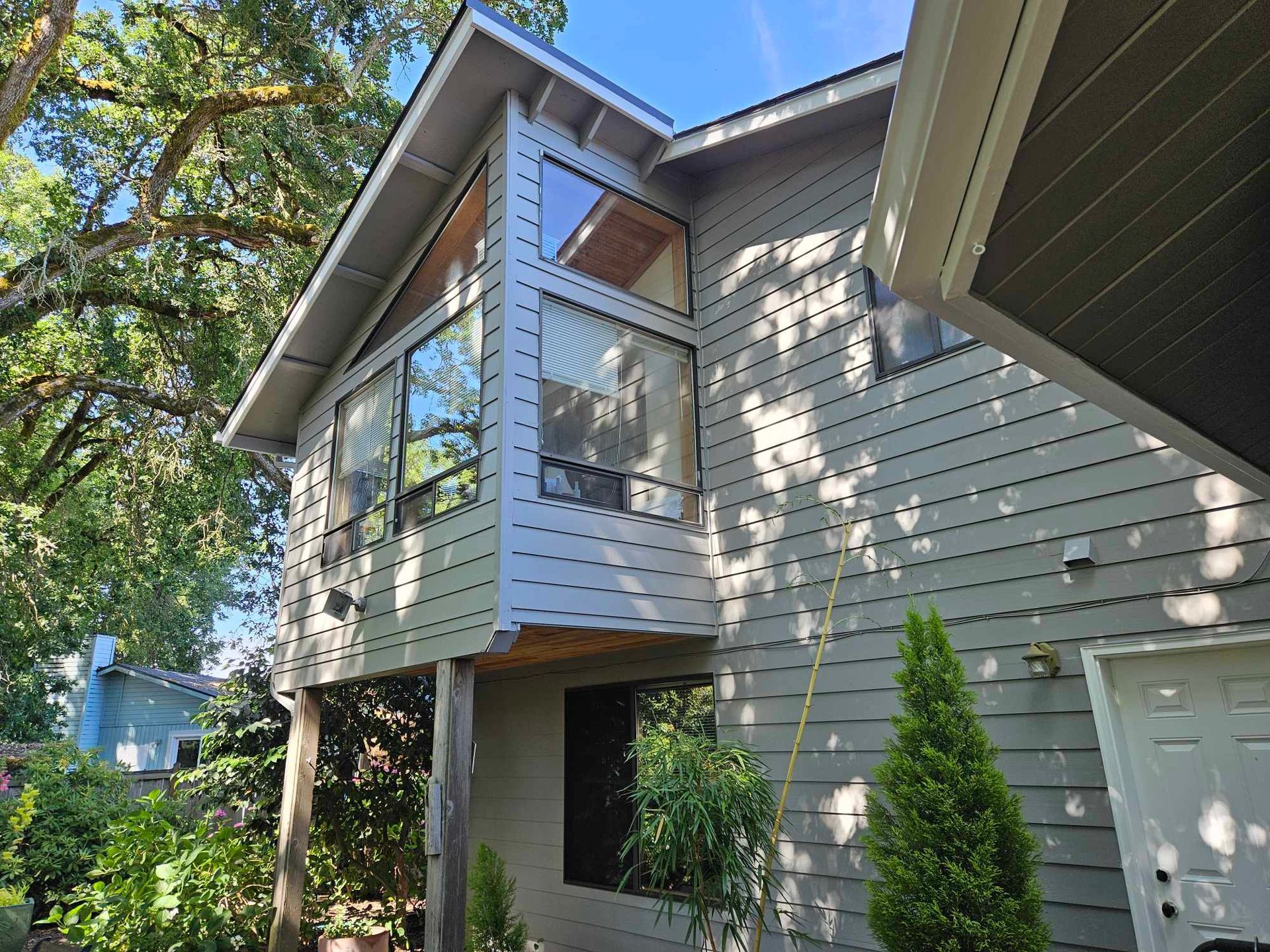 Two-story light gray house with a small balcony and white front door, viewed from the driveway.