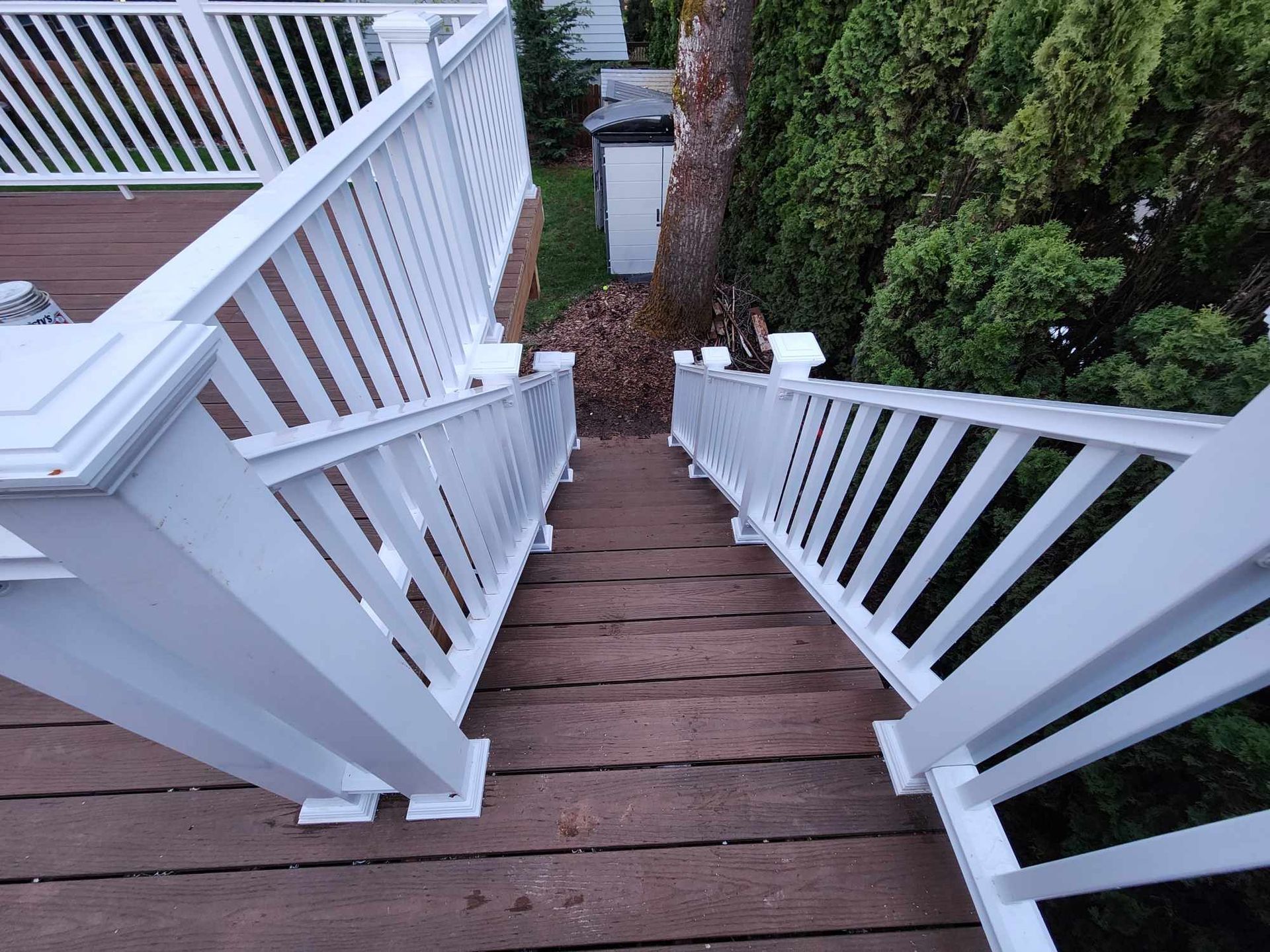 White-railed wooden staircase leading down to a garden path between dense green hedges