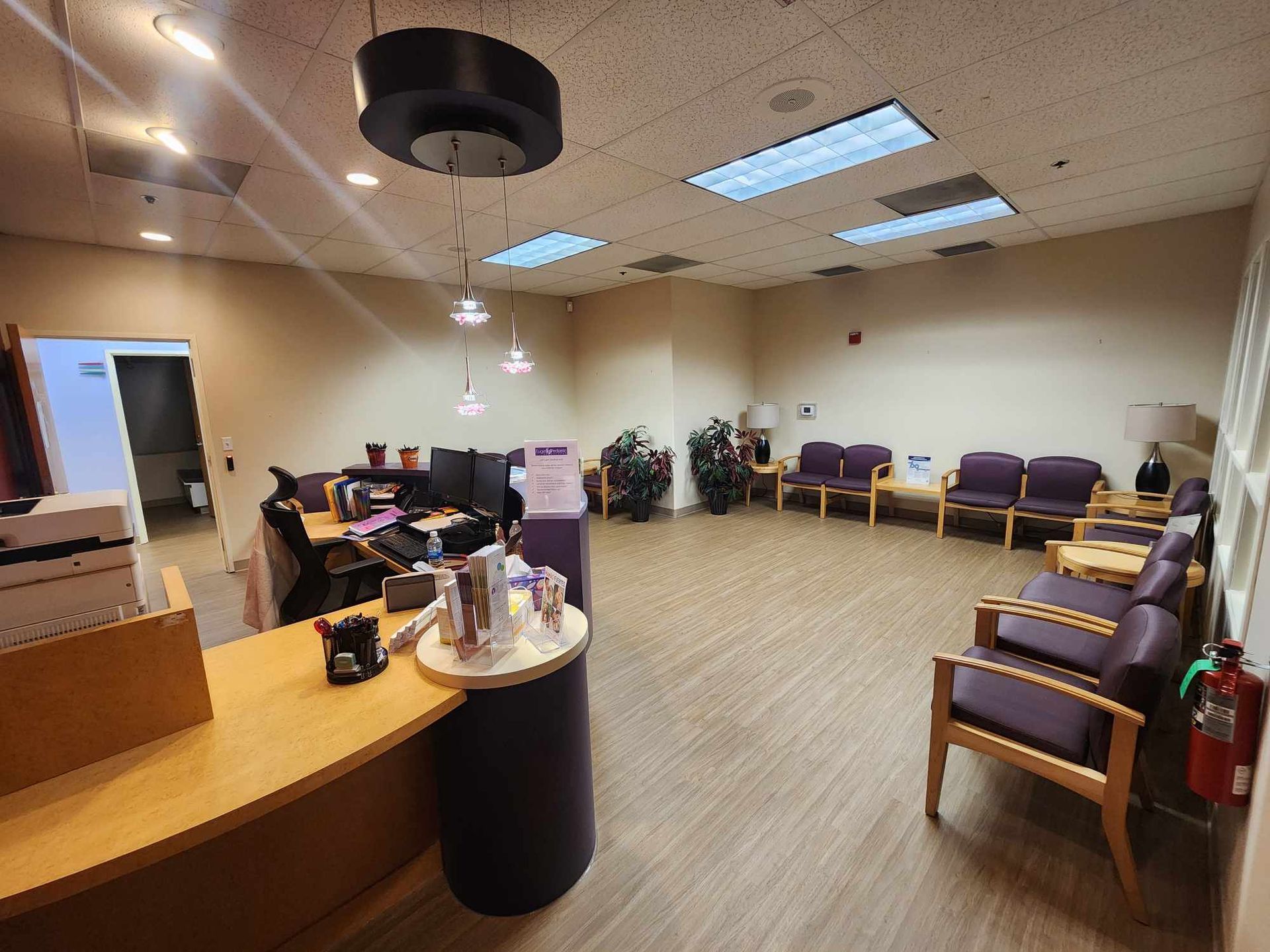 Empty waiting room with purple chairs, reception desk, and overhead lights