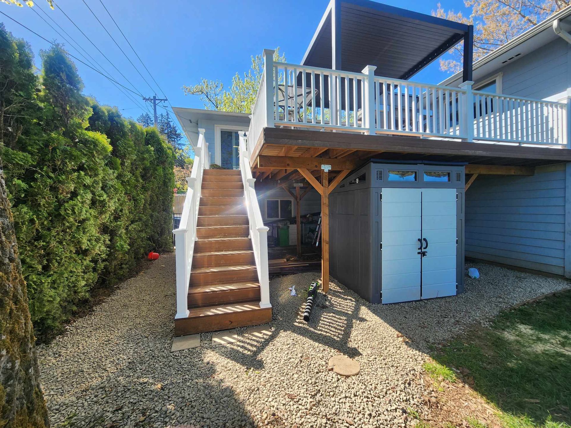 Backyard deck with wooden stairs, white railing, and storage shed beside a gravel path