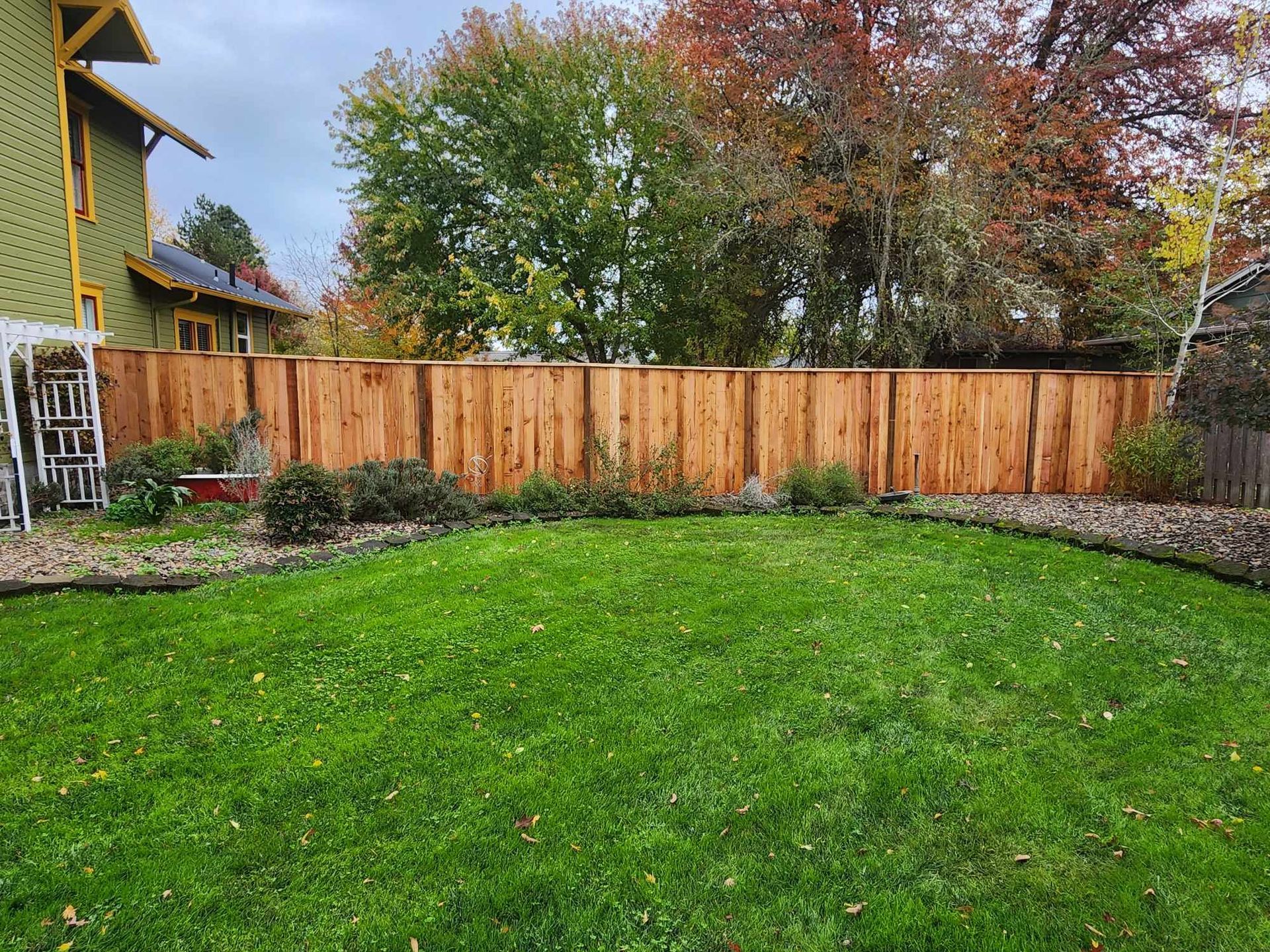 Green backyard lawn with wooden fence, garden beds, and trees in autumn colors