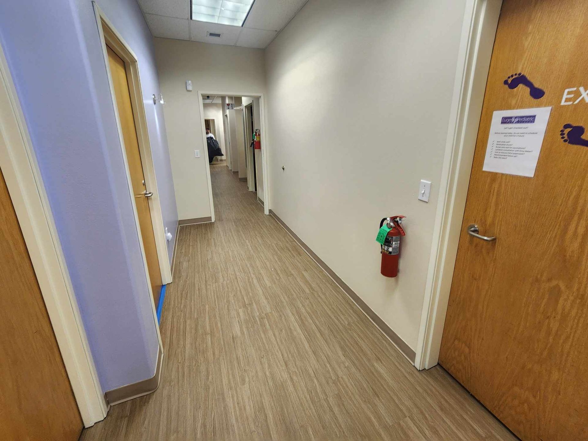 Office hallway with beige carpet, white walls, wooden doors, and a fire extinguisher on the right.