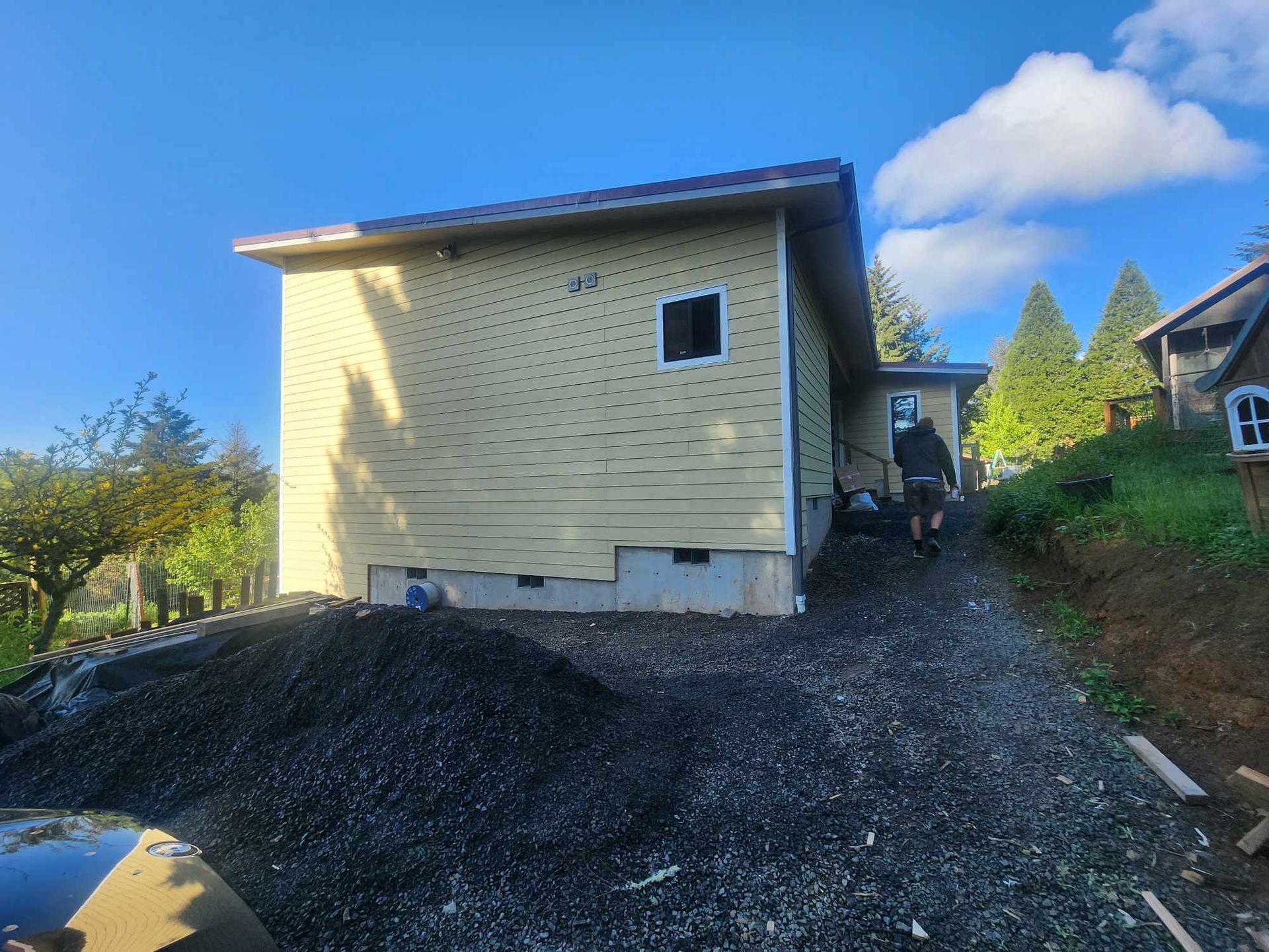 Yellow house on a gravel slope with a small window under a blue sky with clouds.