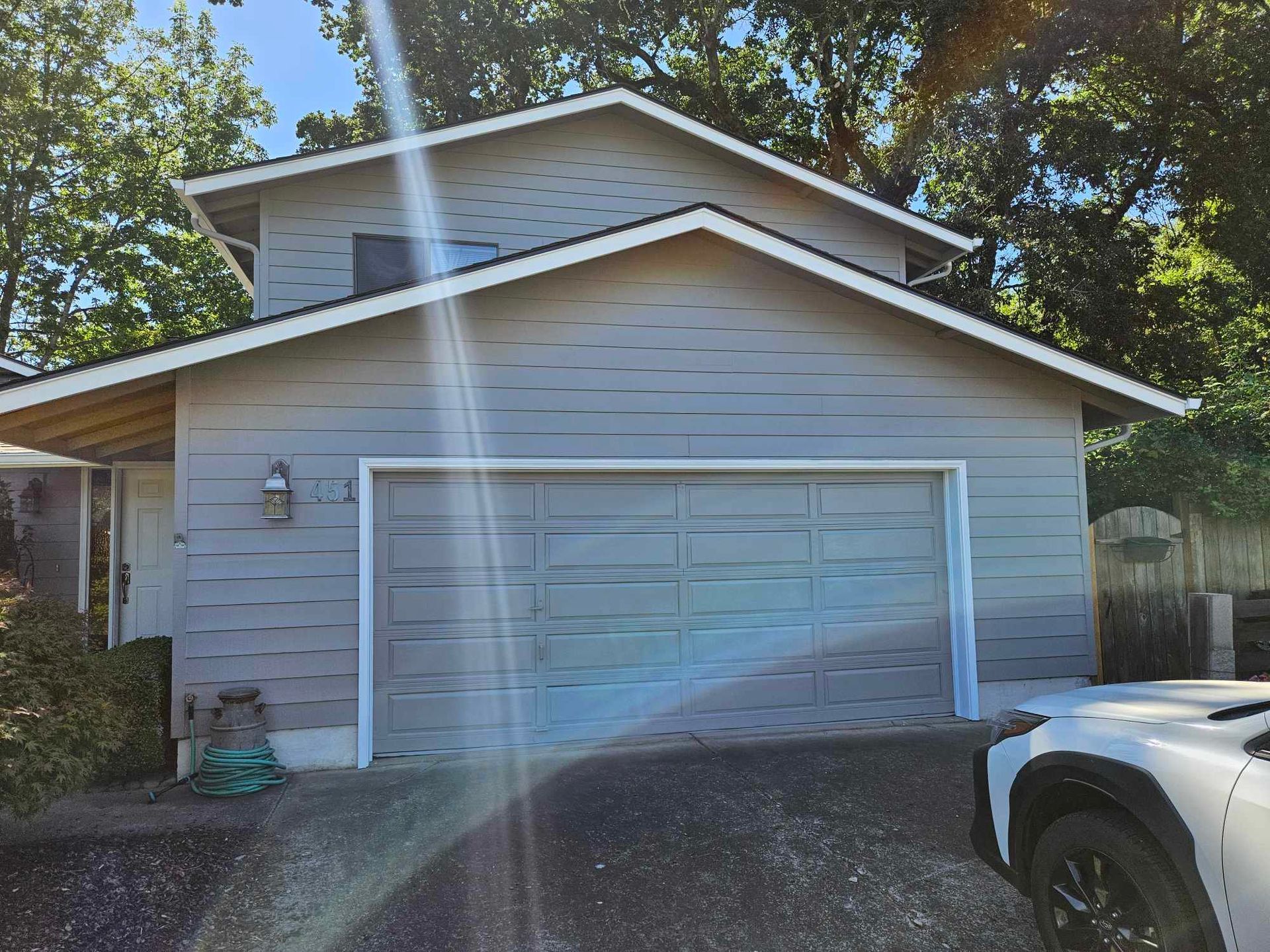Gray detached garage with double doors and sun glare, trees in the background