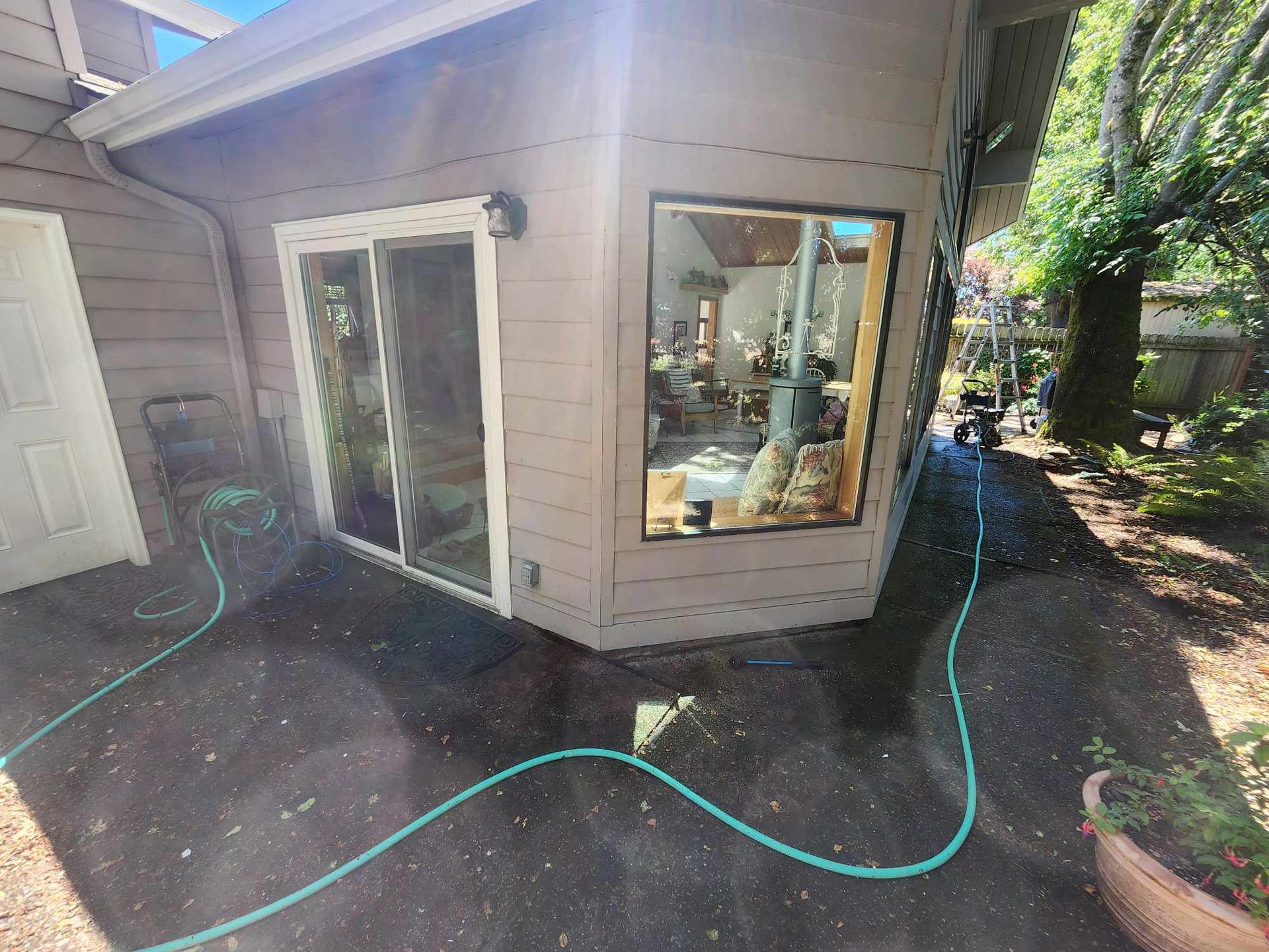 Backyard patio with sliding glass doors, garden hose, and a sunlit window reflecting outdoor furniture.