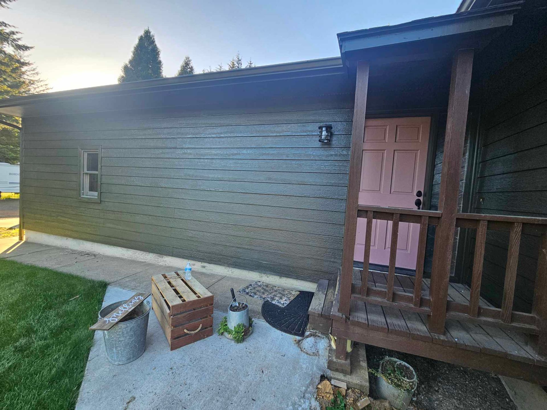 Backyard patio beside a brick house, with a small porch, pink door, and scattered yard items.