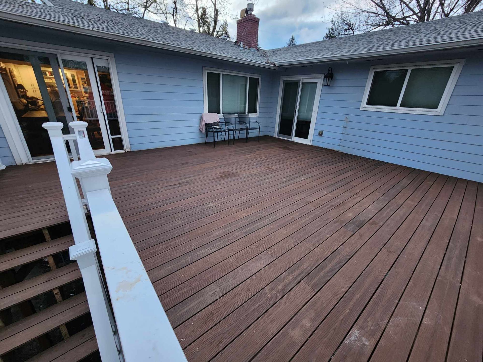 Back patio with brown wooden deck, white railing, and sliding glass doors on a light blue house