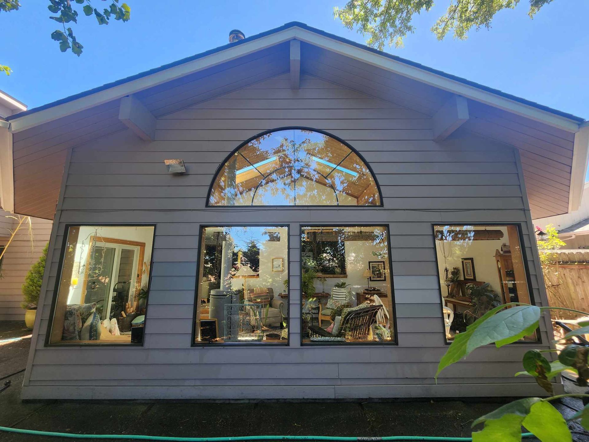 Front view of a small gray house with large windows and a central arched window above the entrance
