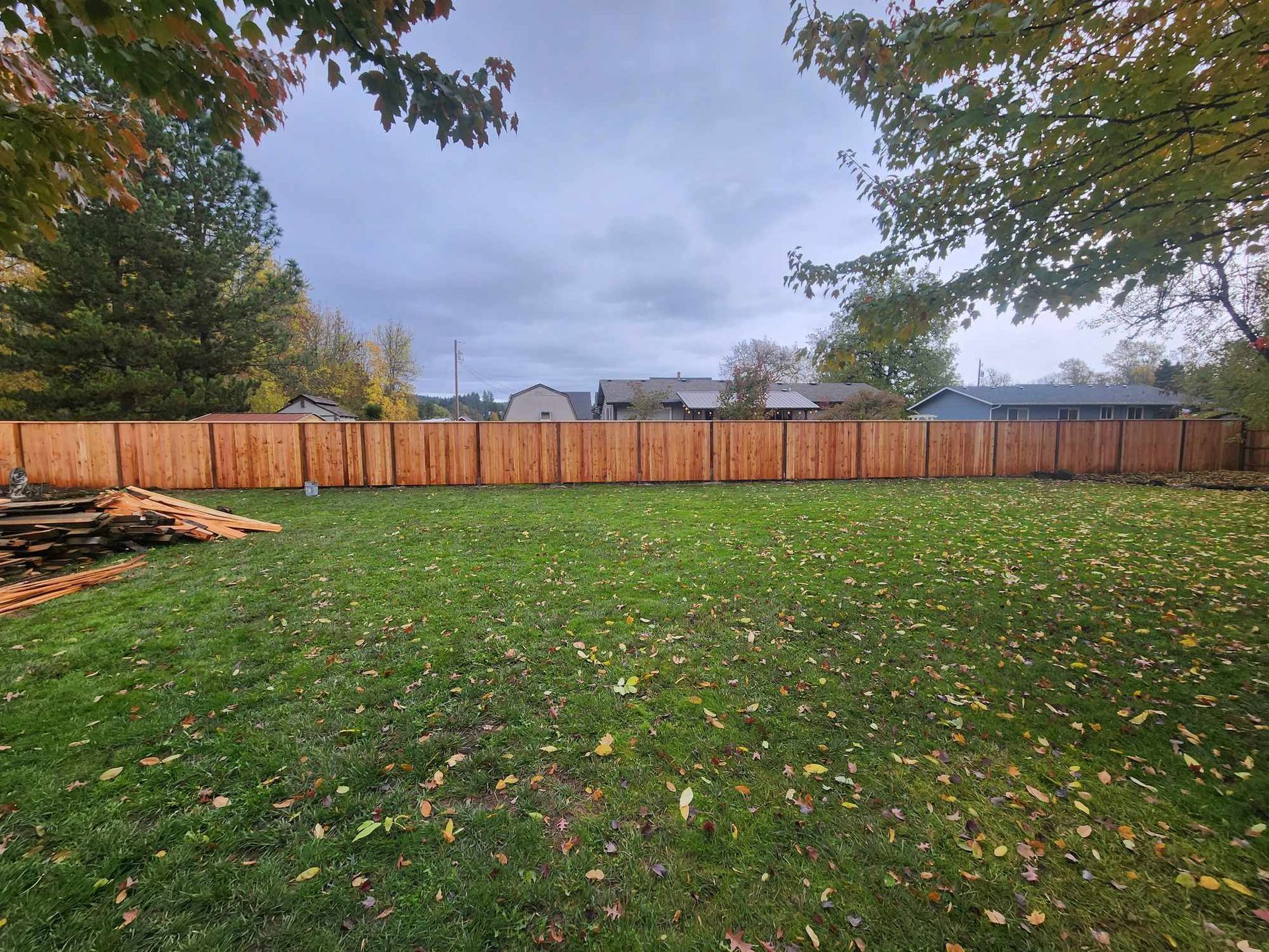 Backyard with green lawn, wooden fence, trees, and a cloudy sky