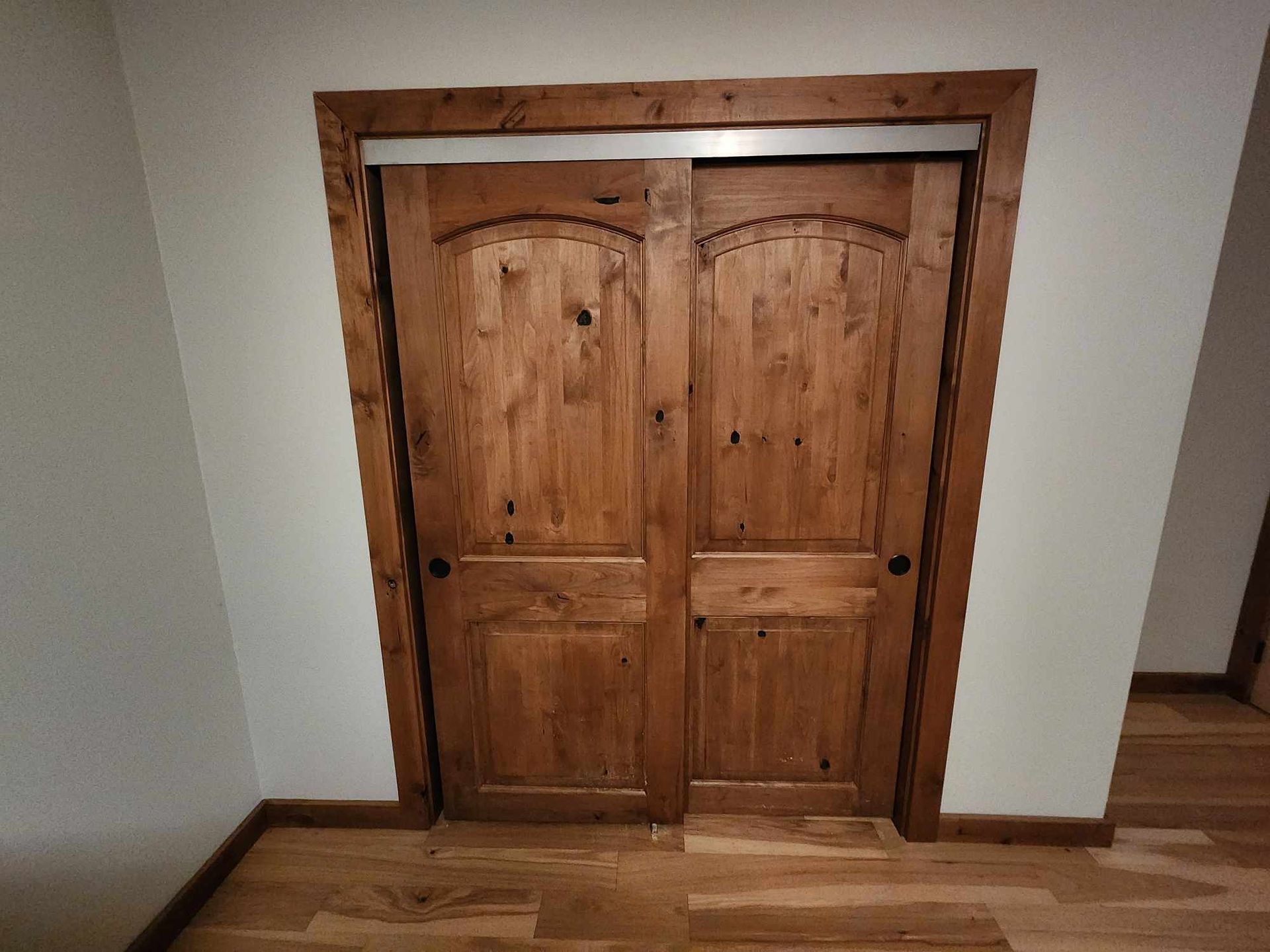 Wooden double doors set in a white hallway wall with wood trim and hardwood floor