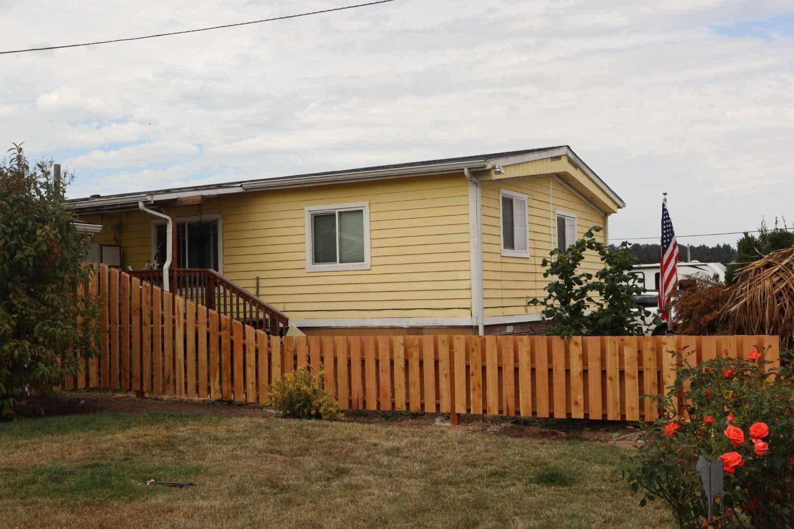 Yellow house with a wooden fence, lawn, and an American flag in the yard.