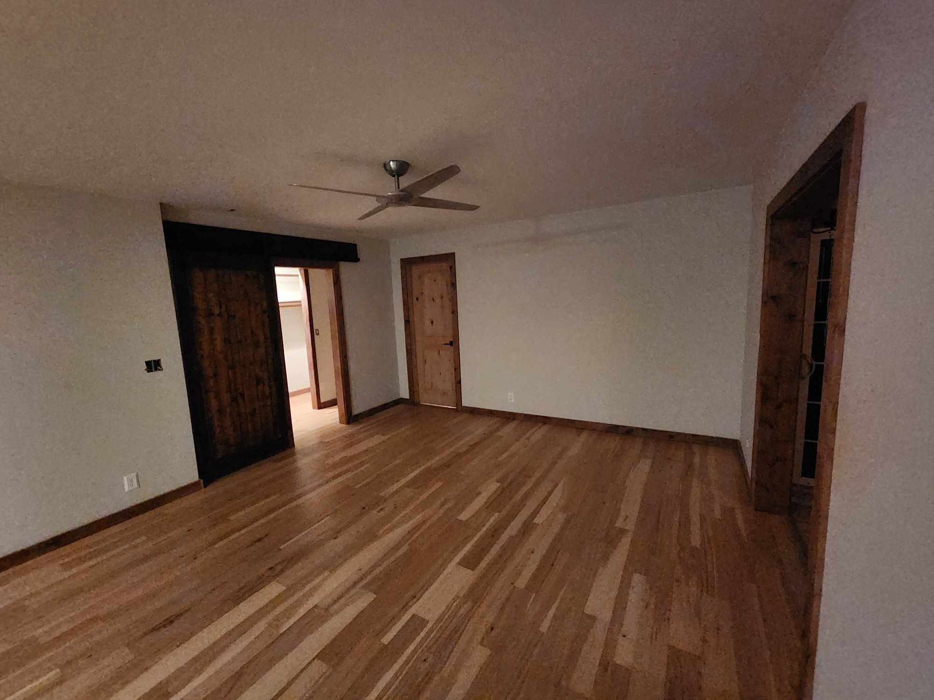 Empty room with hardwood floors, white walls, ceiling fan, and three wooden doors.