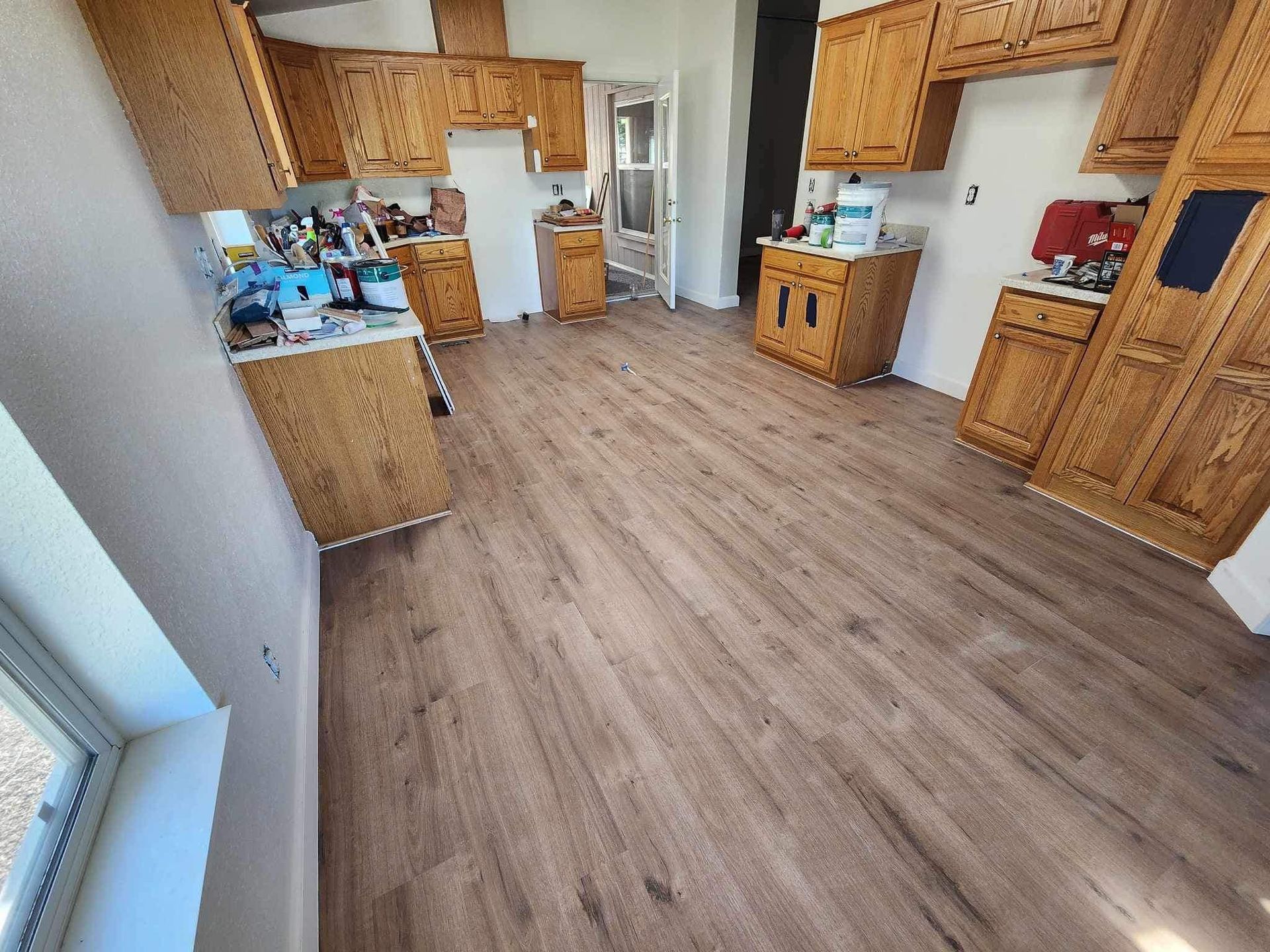Empty kitchen with wood cabinets, light wood floor, and a window on the left.