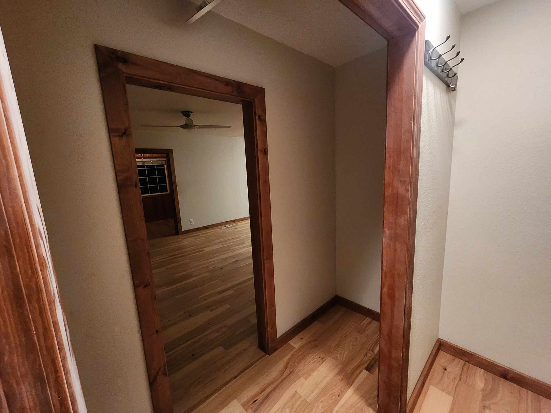 Wooden hallway with doorways, white walls, and wood trim leading into a room with wood flooring.