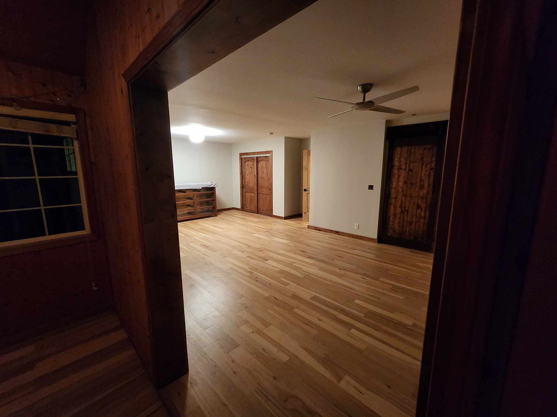 Empty living room with hardwood floors, white walls, and wooden doors, viewed from a doorway