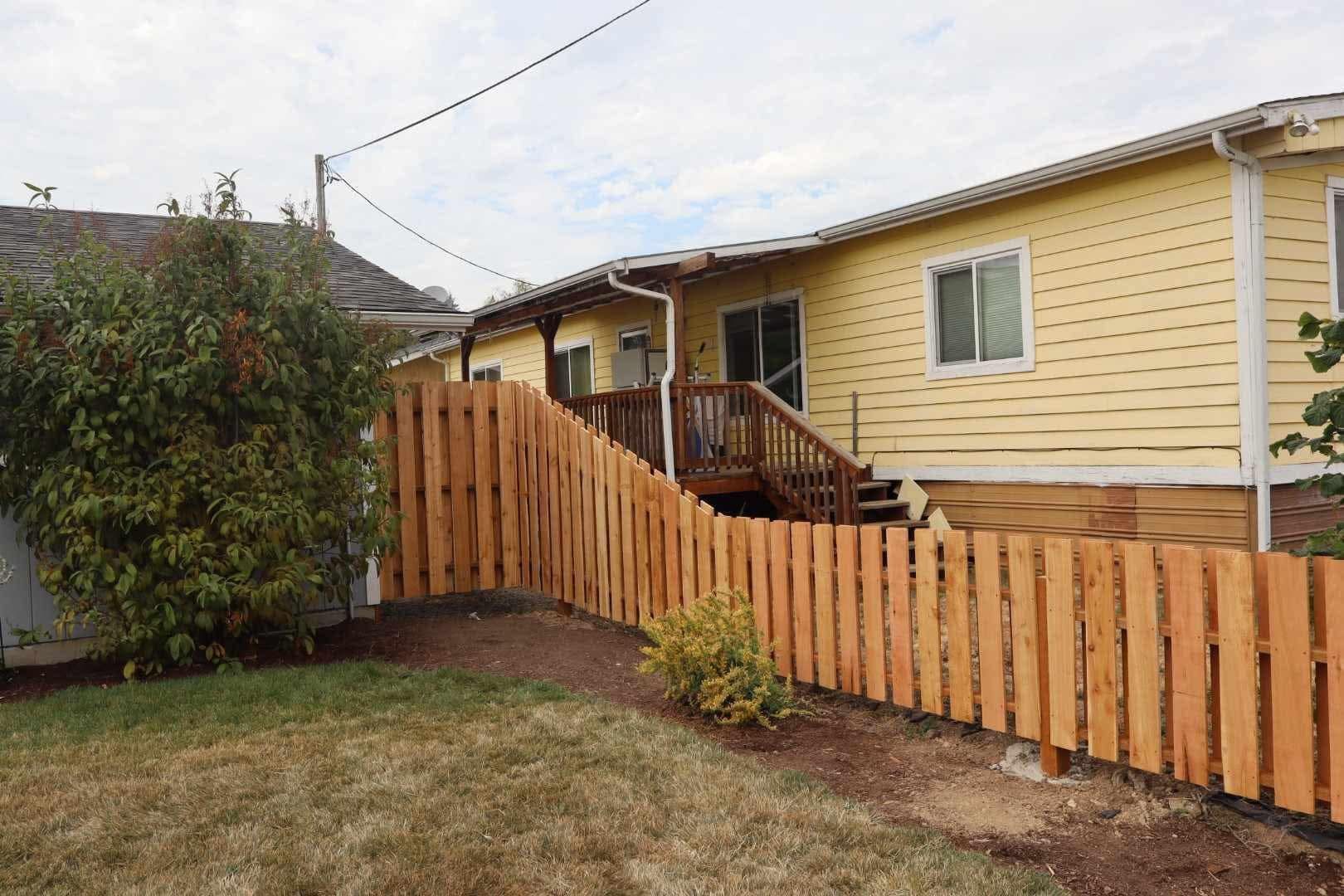 Single-story yellow house with wooden deck, picket fence, and front yard lawn