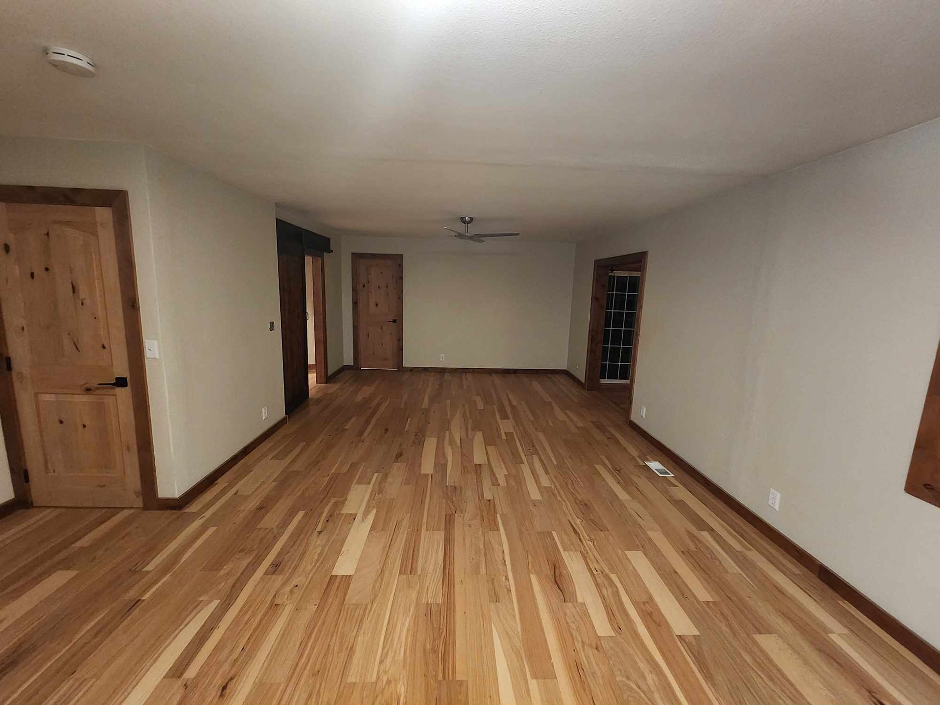 Empty room with wood floors, beige walls, and several wooden doors.