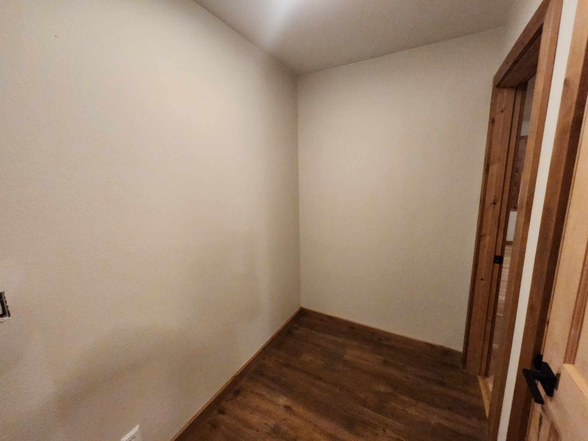 Empty beige room with hardwood floor and open wooden door trim