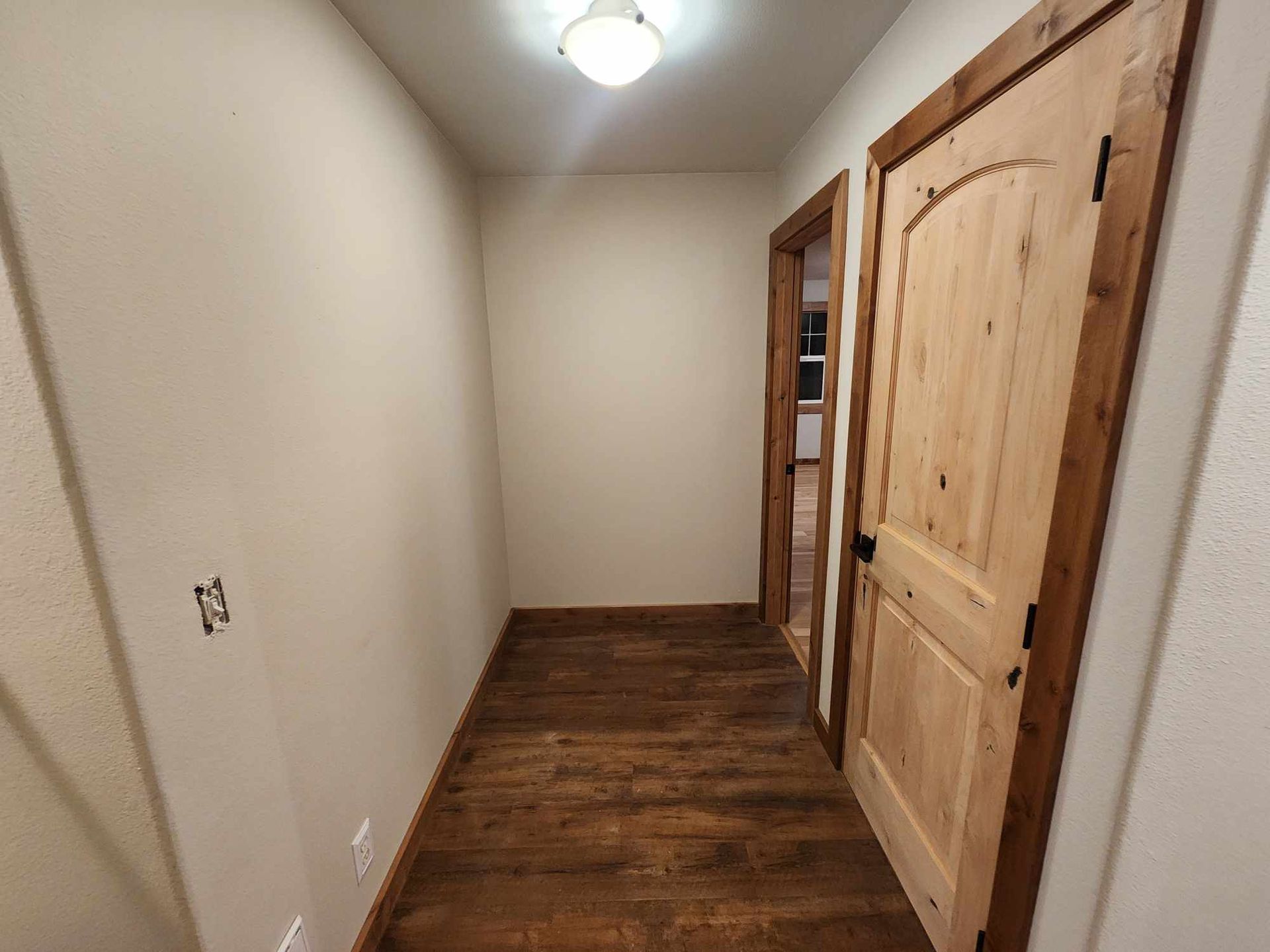 Narrow hallway with wood floor, beige walls, ceiling light, and closet doors on the right.