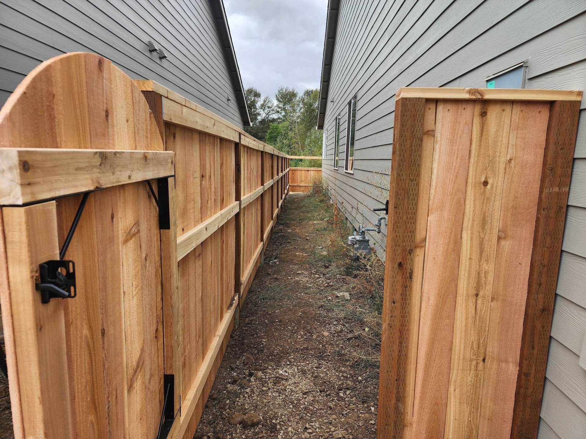 Narrow gravel alley between two houses, with wooden fences and gates on both sides.