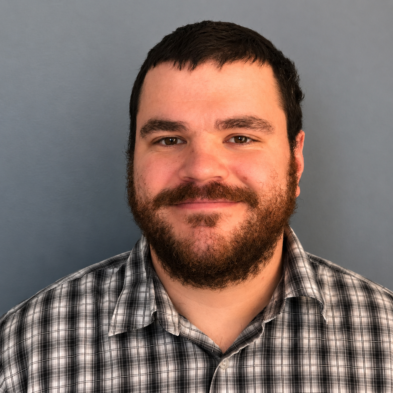 Portrait of a smiling man with a beard wearing a plaid shirt against a gray background