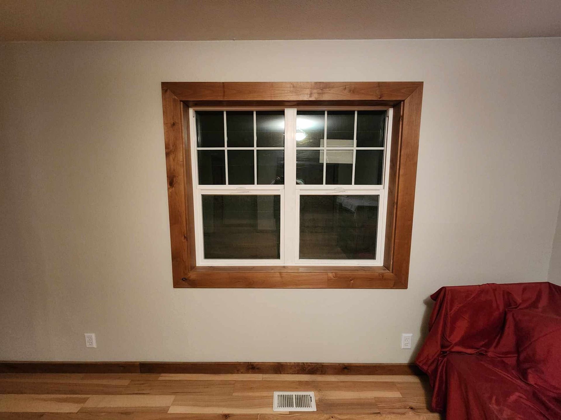 Bare room with a large window, wood trim, and a red-covered couch on the right.