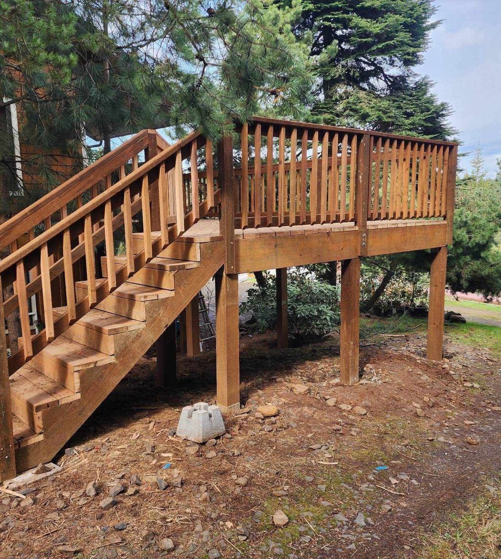 Wooden staircase leading to a raised deck with railings in a wooded backyard garden