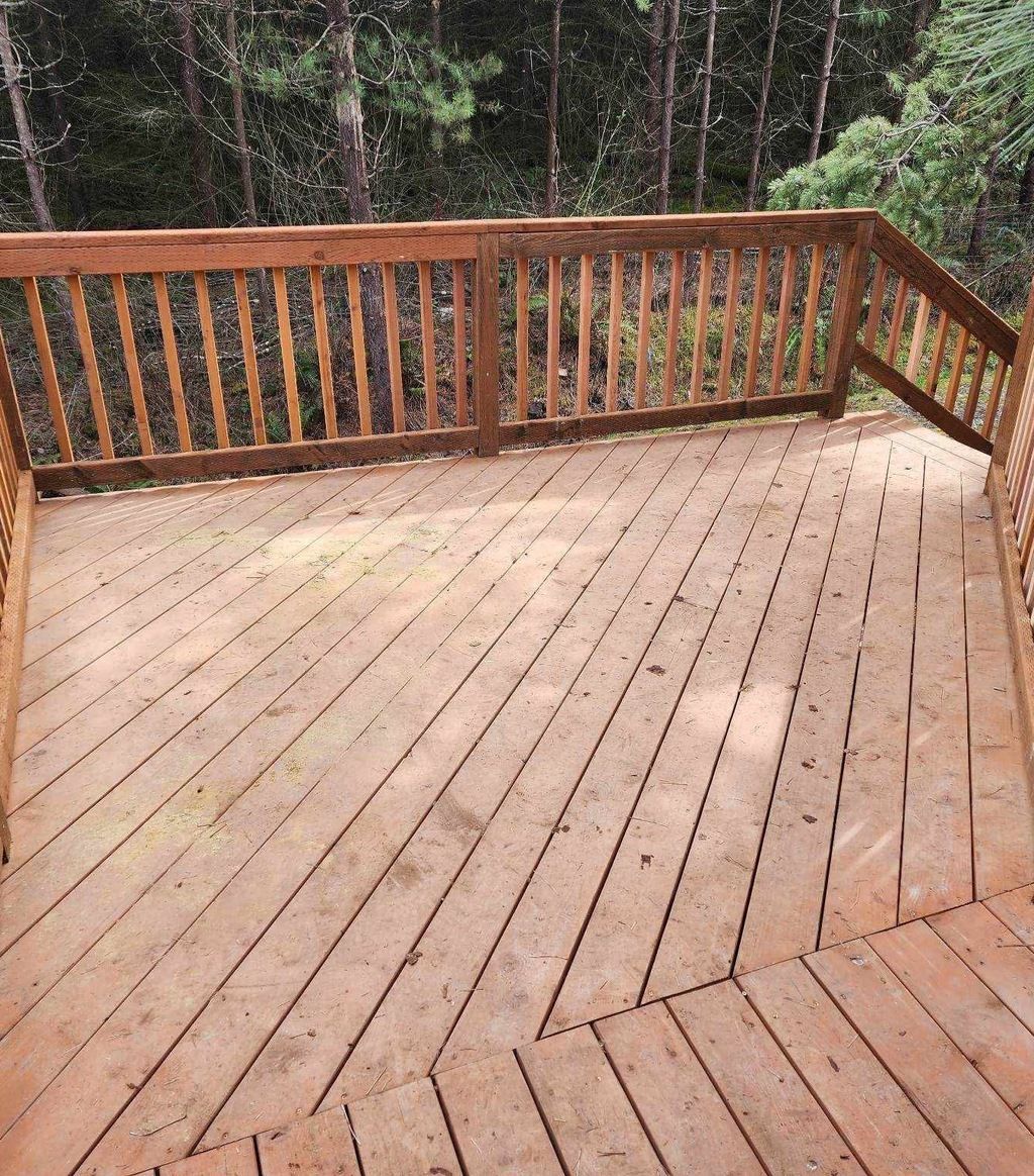 Wooden deck with railing overlooking a wooded area, viewed from a corner.