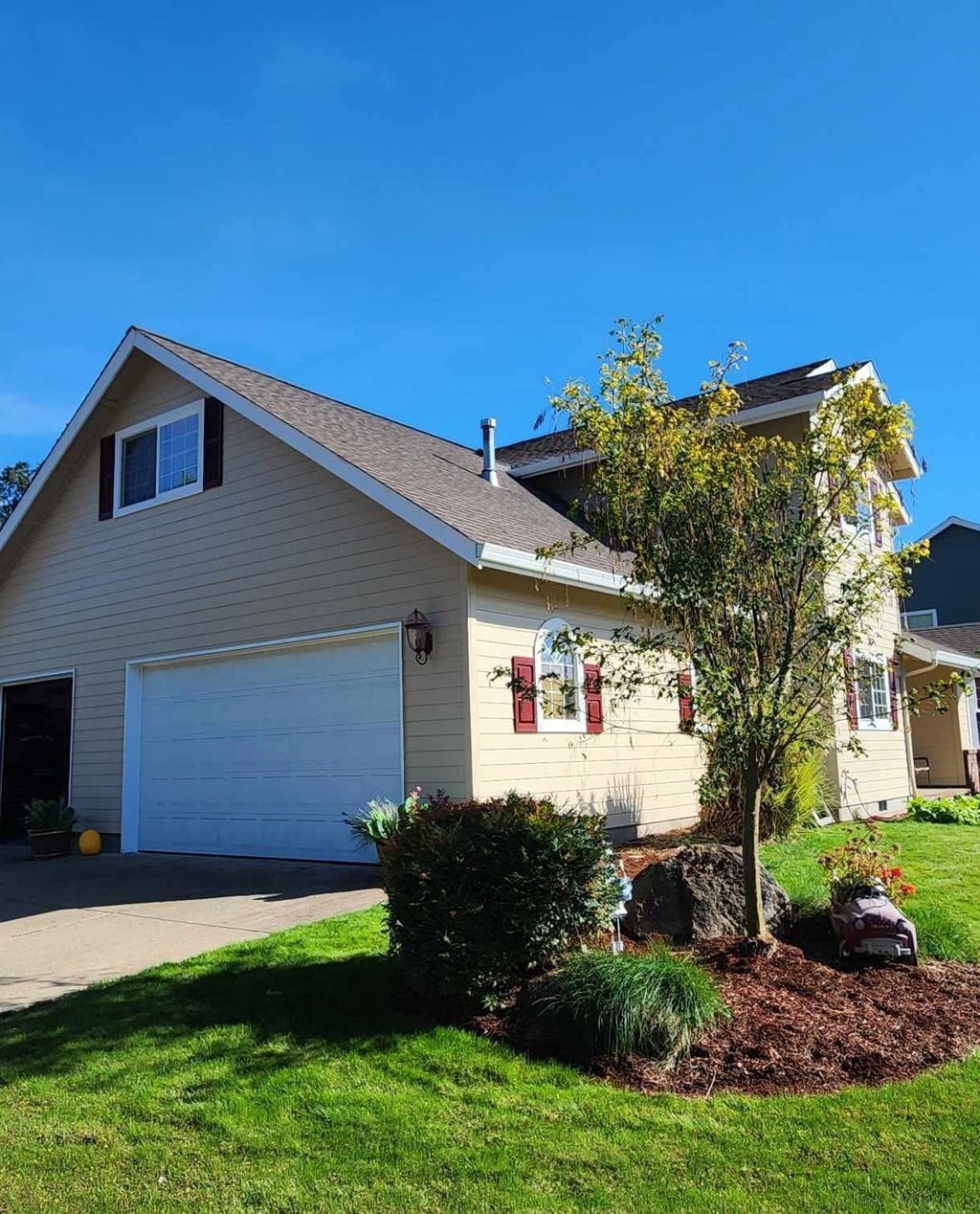 Suburban house with beige siding, white garage, and landscaped front yard under a clear blue sky