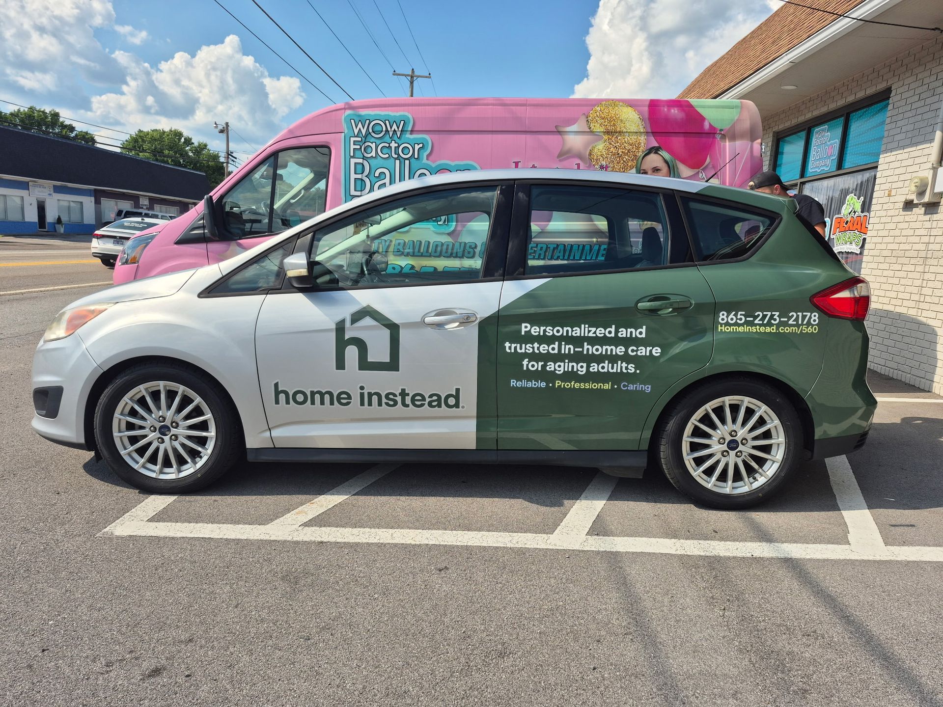 A green and white car is parked in a parking lot next to a pink van.