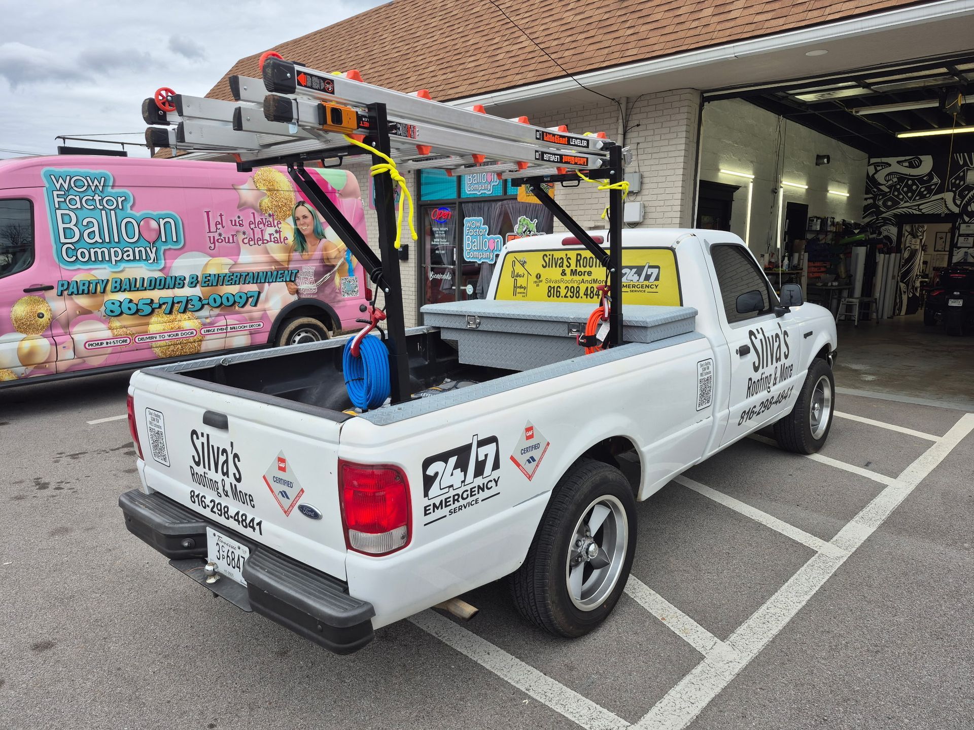 White pickup truck with ladder rack, tool box, and business logo parked outside a building.