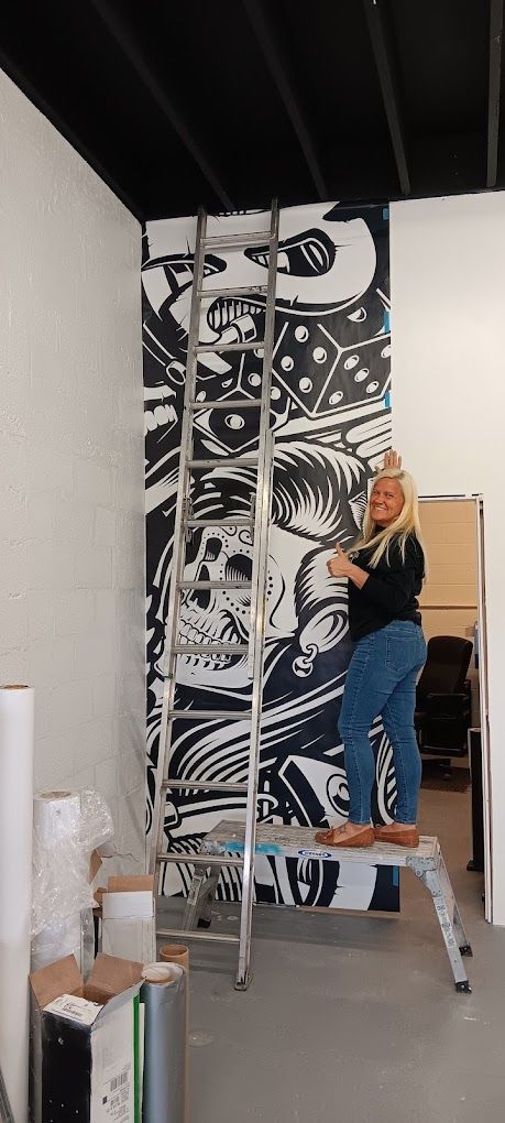 A woman is standing on a ladder in front of a mural on a wall.