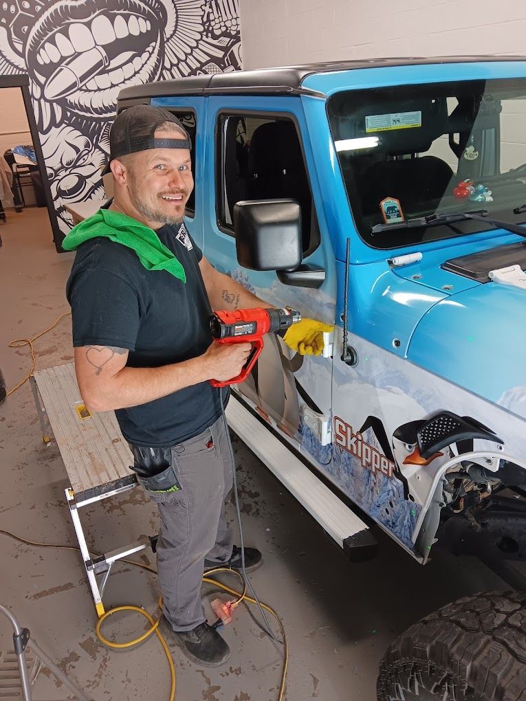 A man is standing next to a blue jeep in a garage.