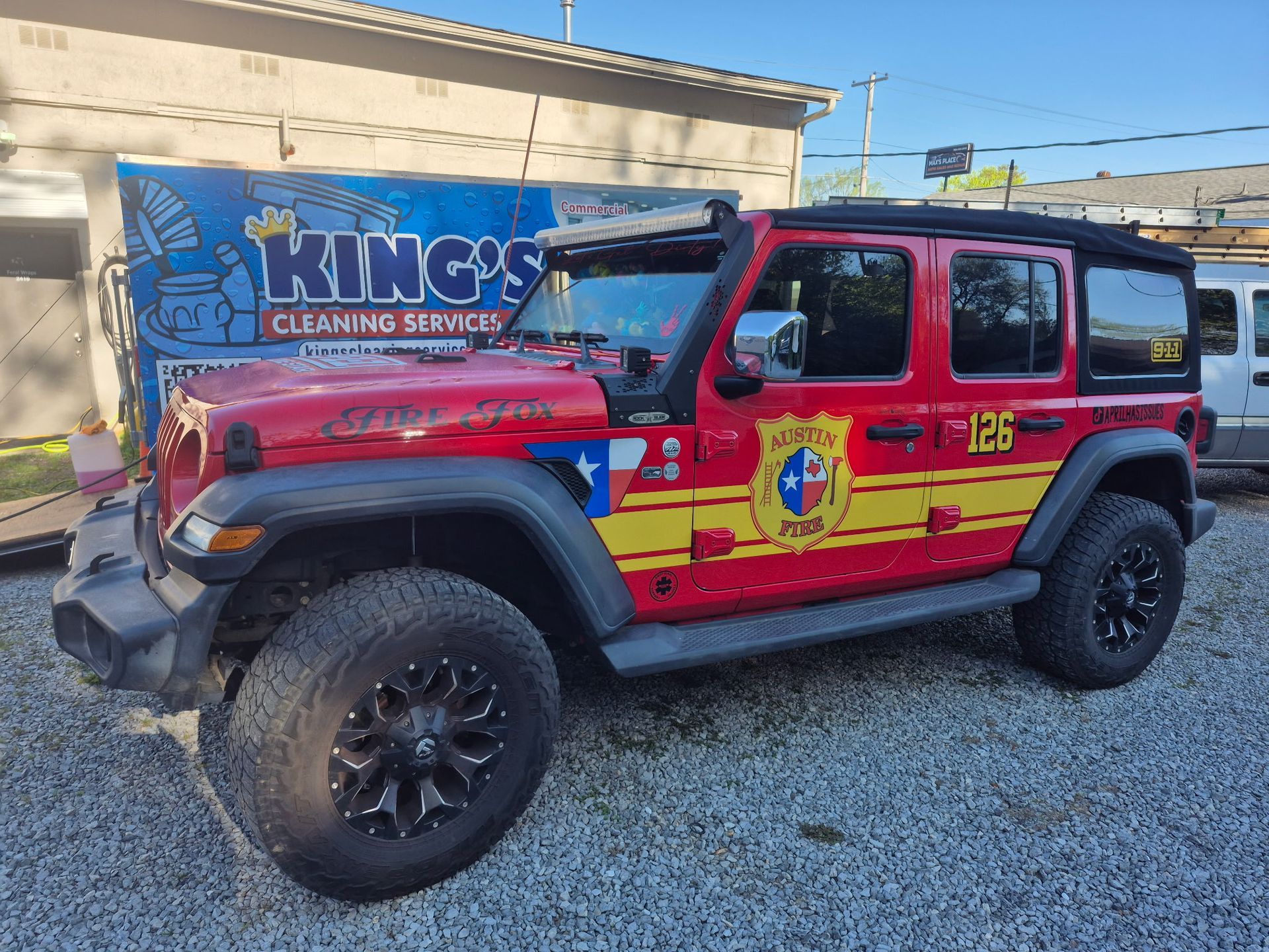 A red jeep is parked in front of a king 's cleaning service truck.
