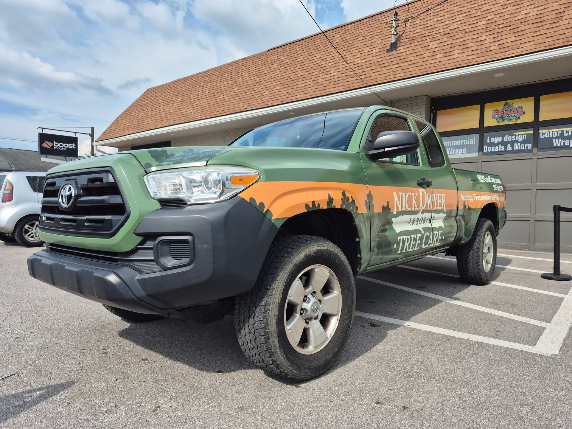 A green and orange truck is parked in a parking lot in front of a building.