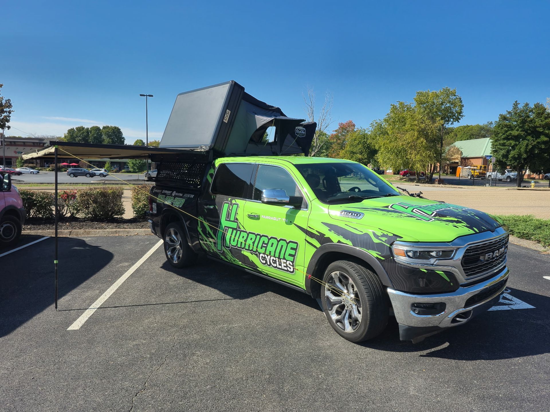 Green and black truck with a pop-up camper in a parking lot with an awning extended.