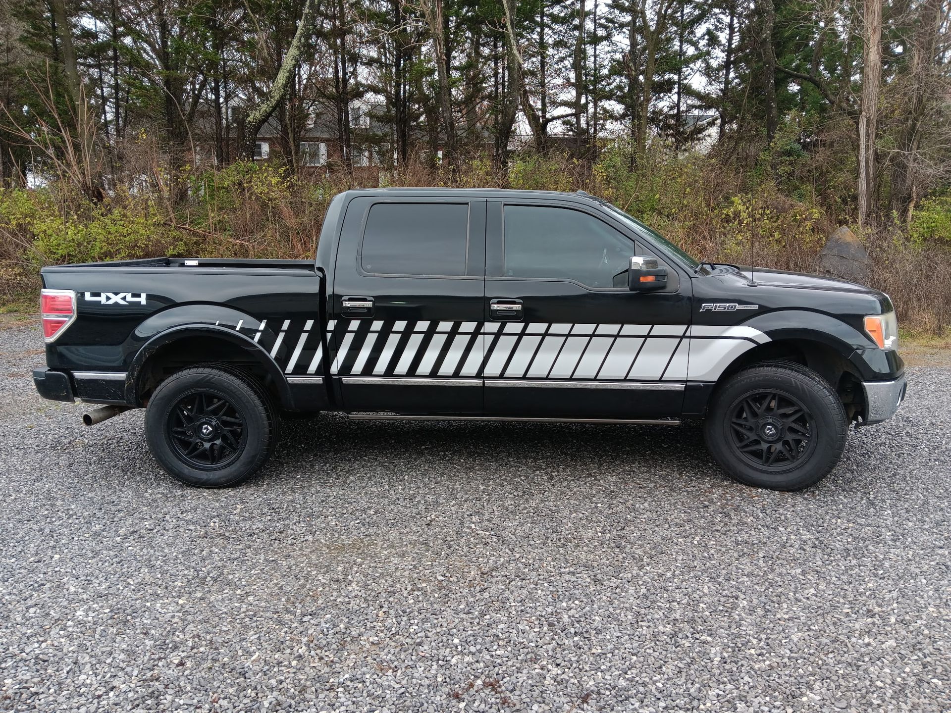 A black ford f150 truck is parked in a gravel lot.
