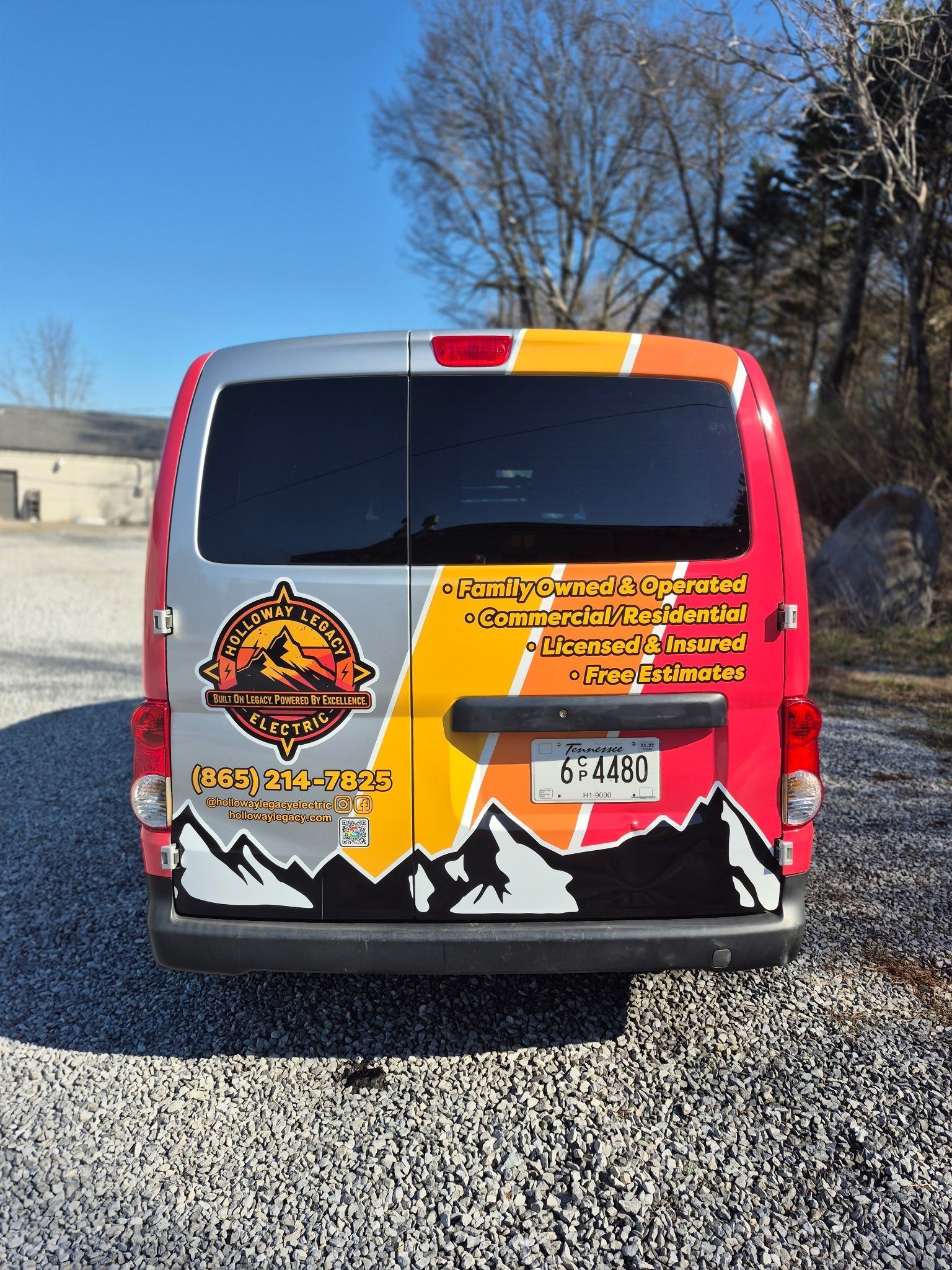 Back of a van with company logo and mountain graphic in a gravel parking lot.