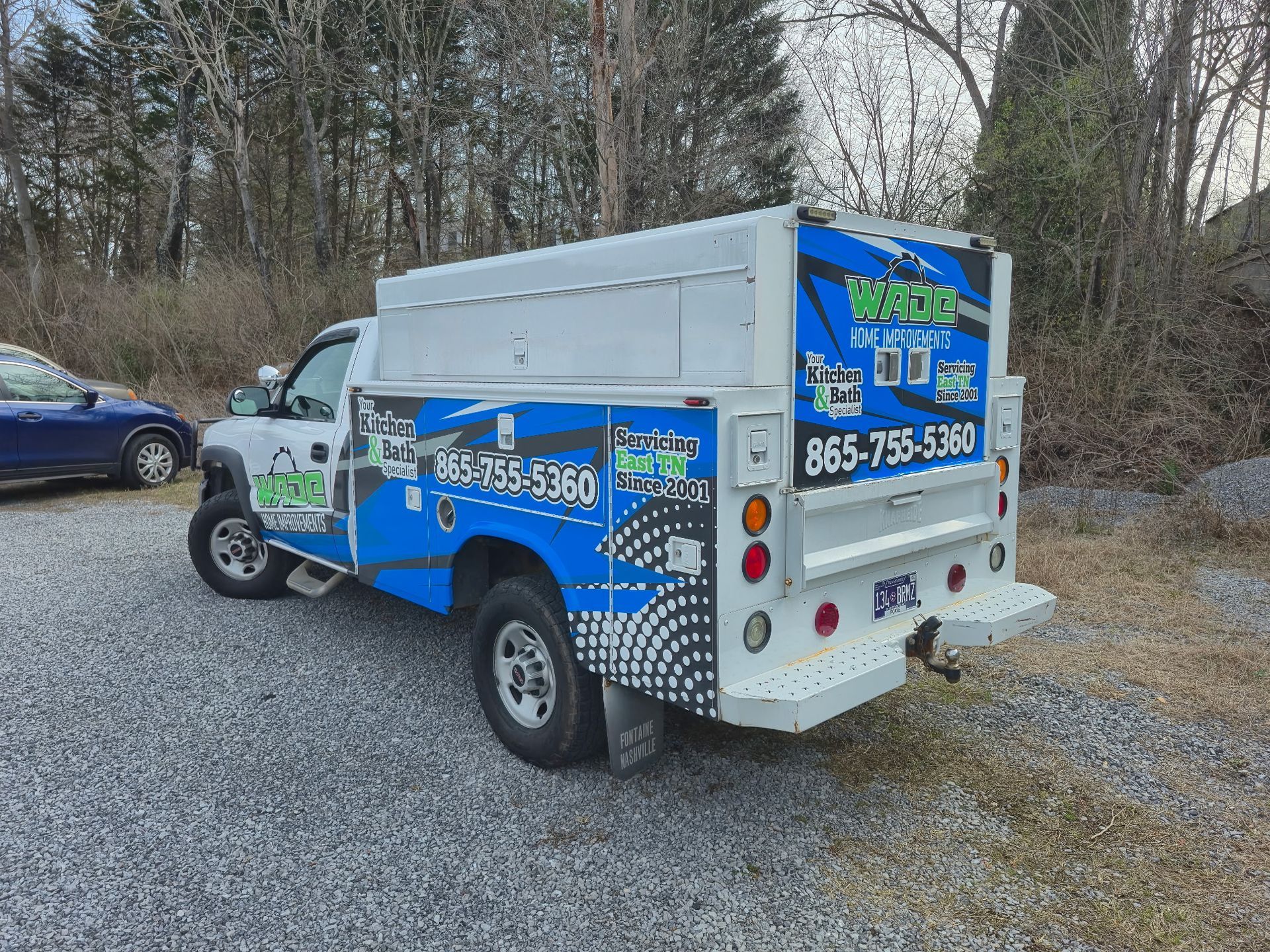 White work truck with blue and green branding, parked on gravel.