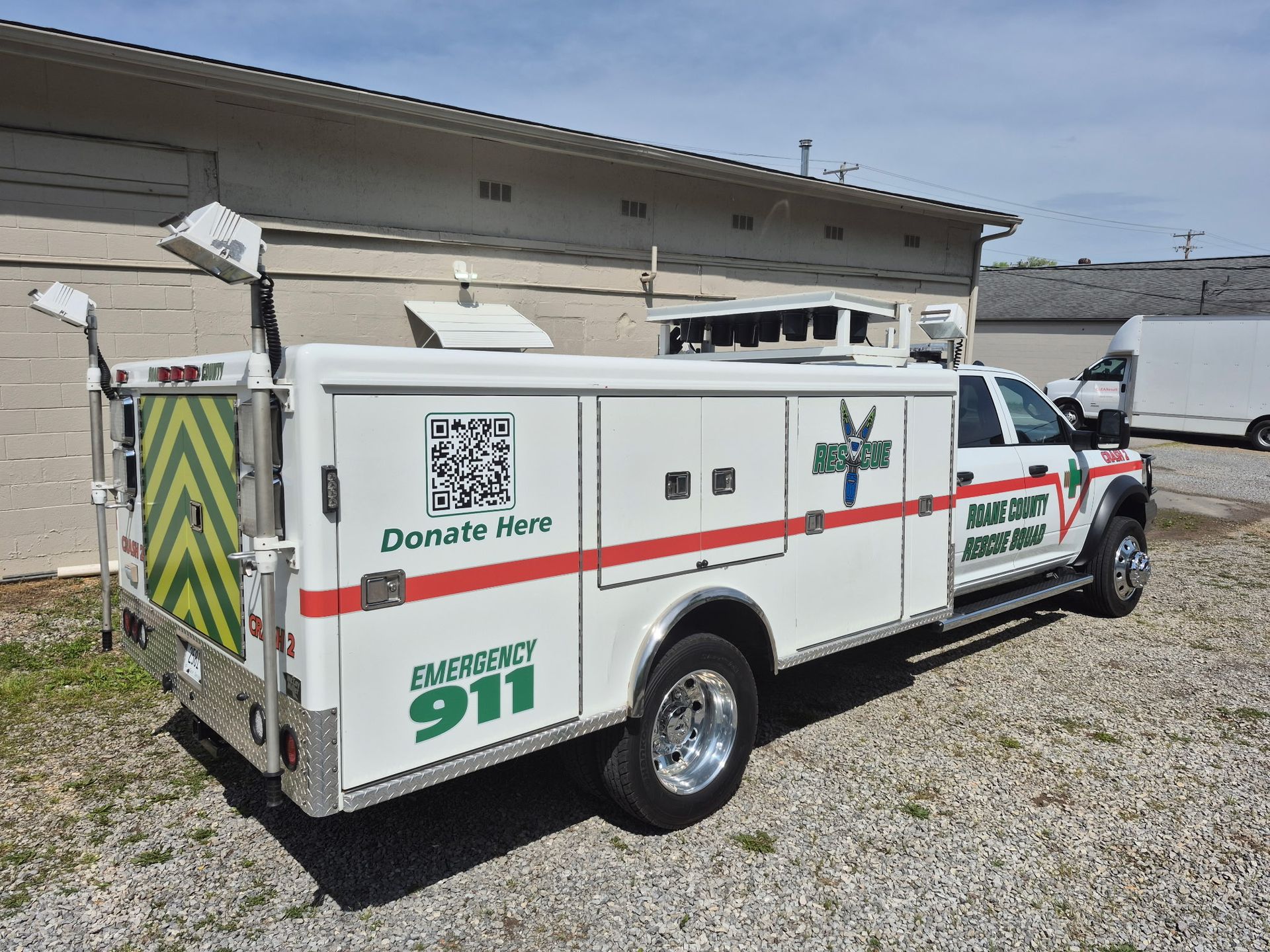 A white ambulance is parked in a gravel lot in front of a building.