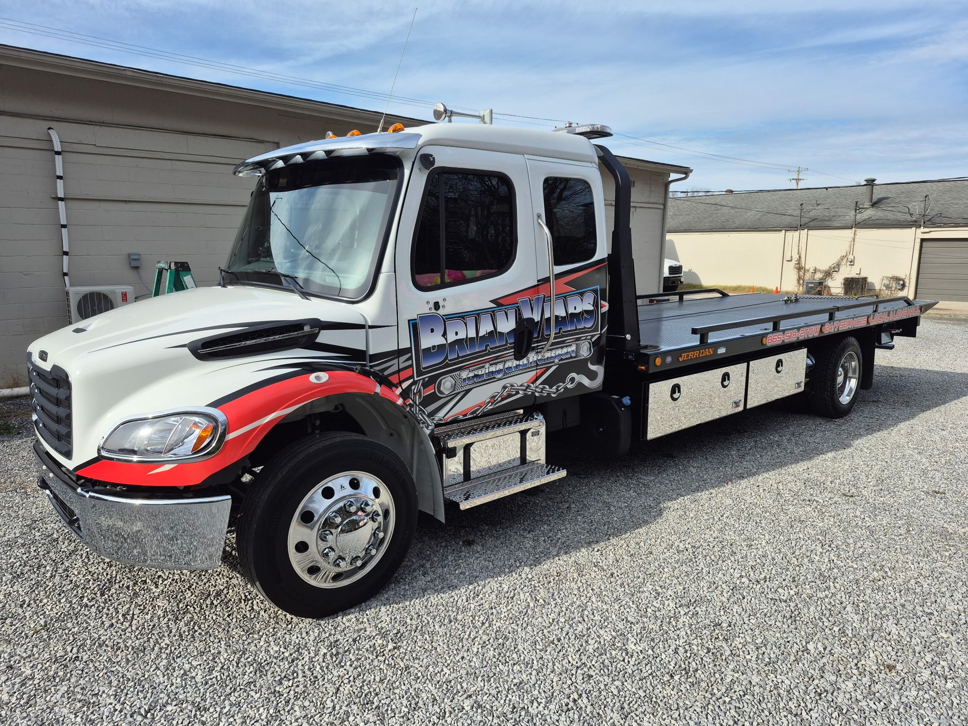 Tow truck, white cab with red and black graphics, parked on gravel.