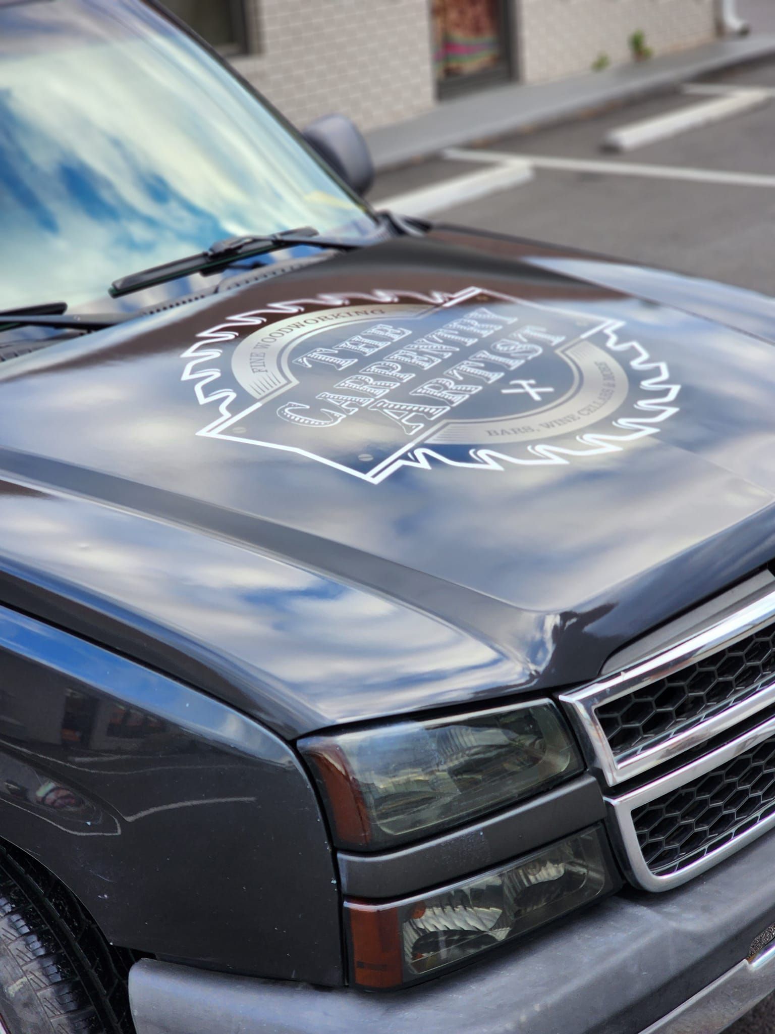 A black truck with a logo on the hood is parked on the side of the road.