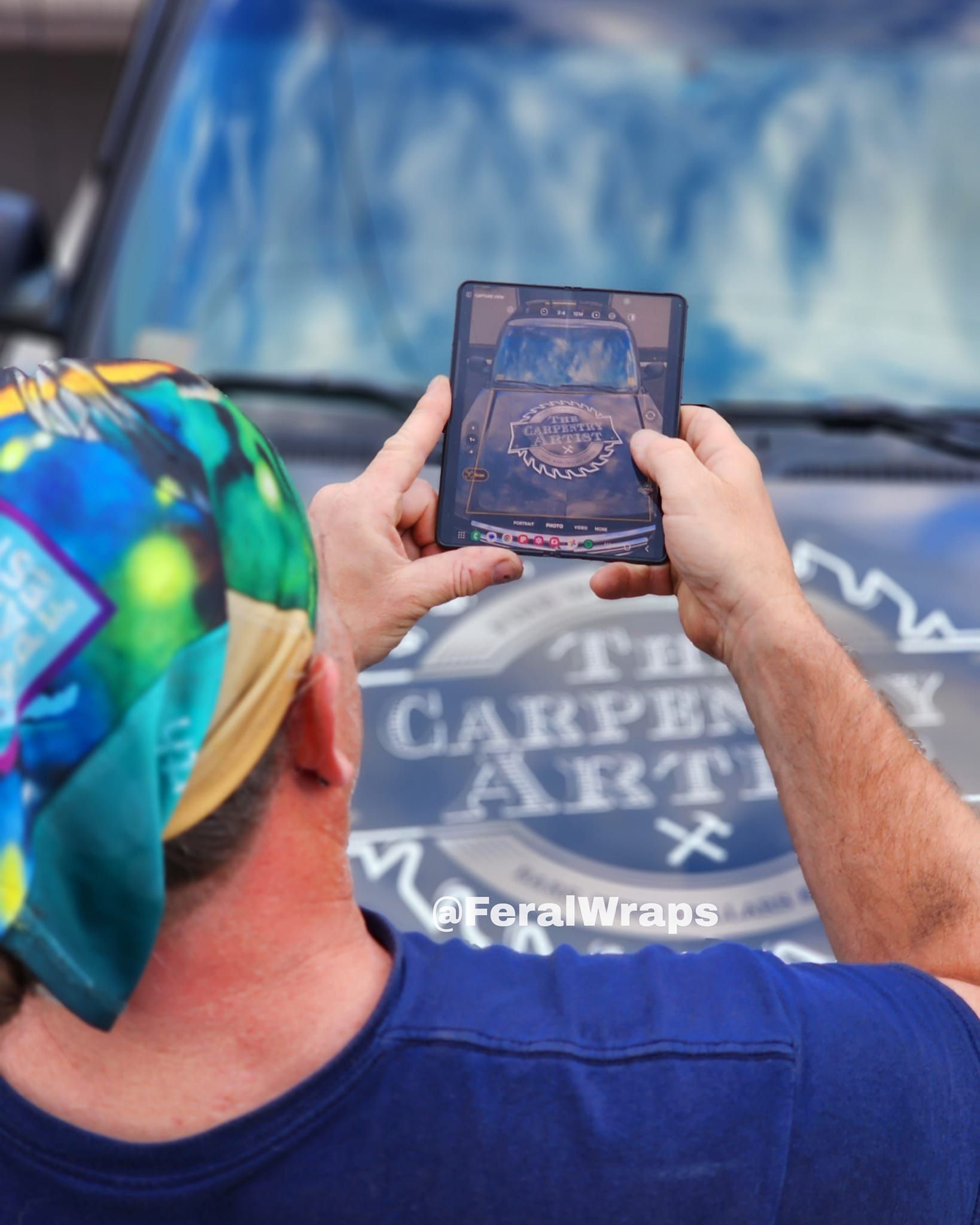 A man wearing a bandana is taking a picture of a car
