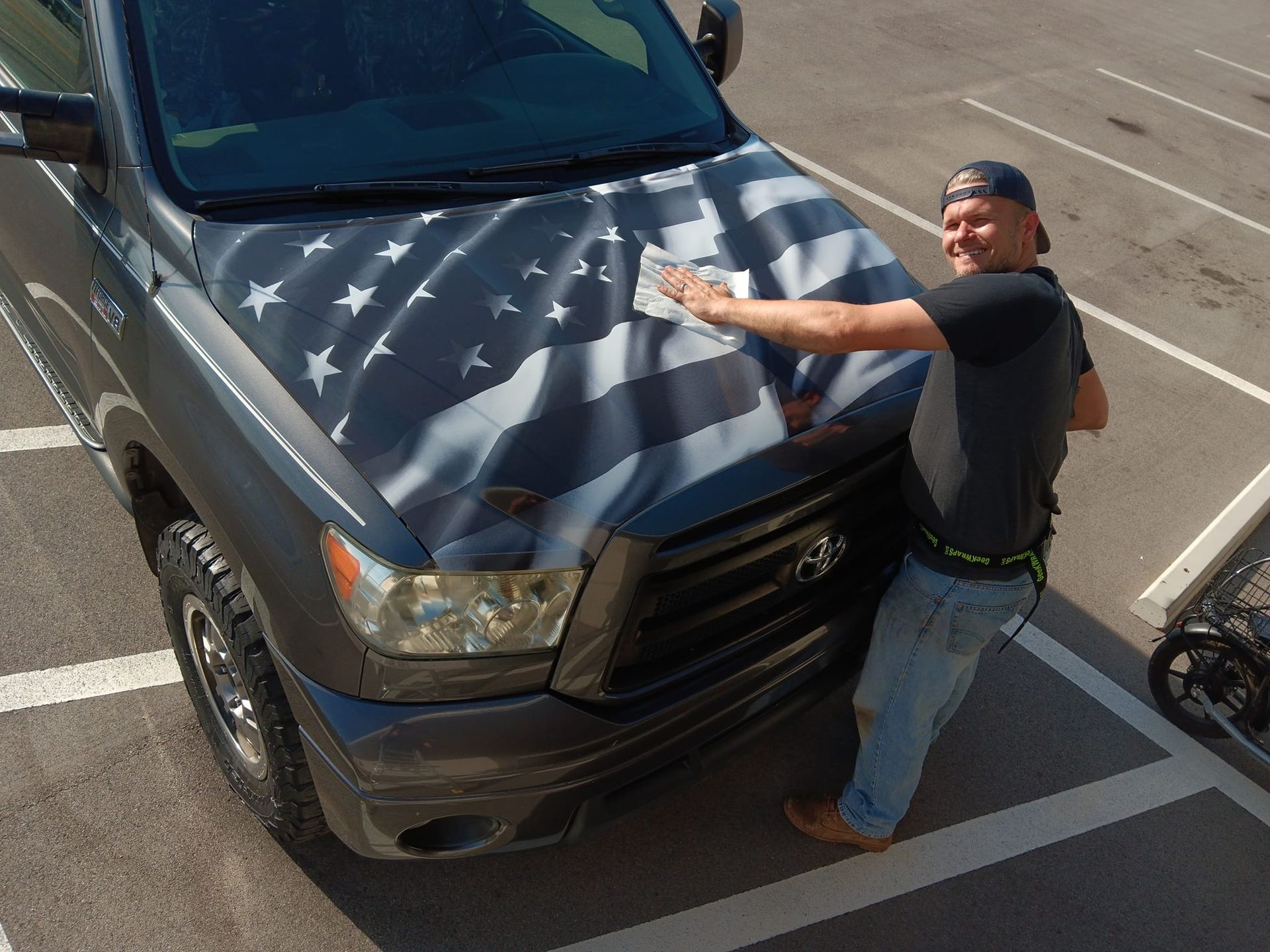 A man is wrapping the hood of a truck with an american flag