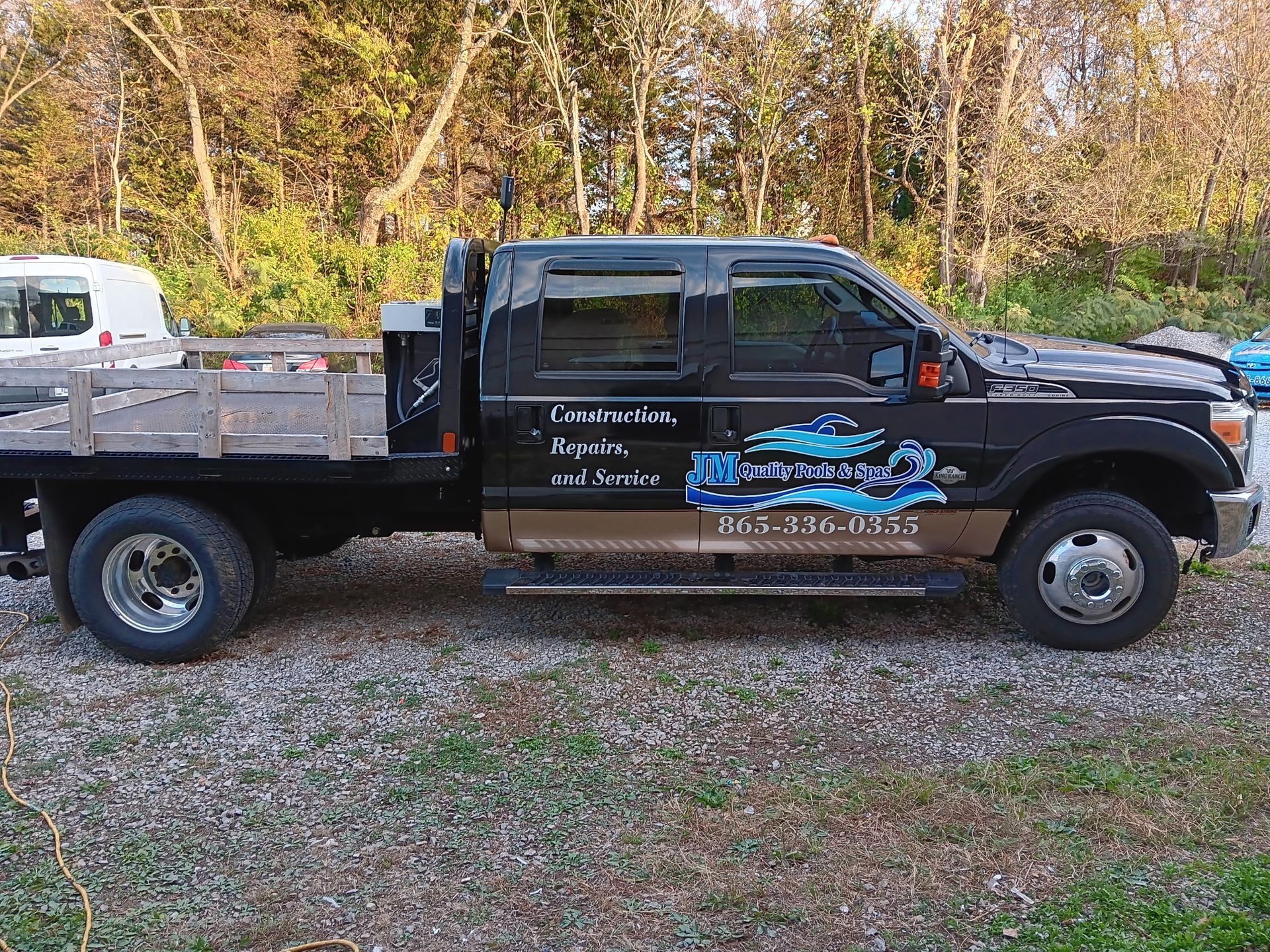 A black truck with a wooden bed is parked in a gravel lot.