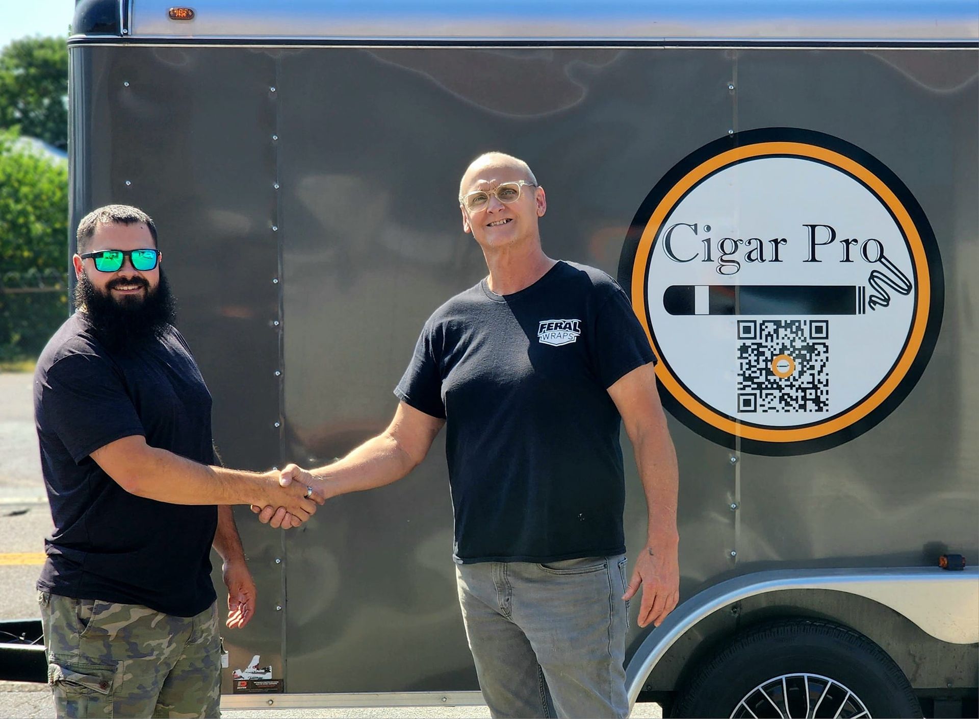 Two guys shaking hands in front of trailer with vinyl logo on the side.