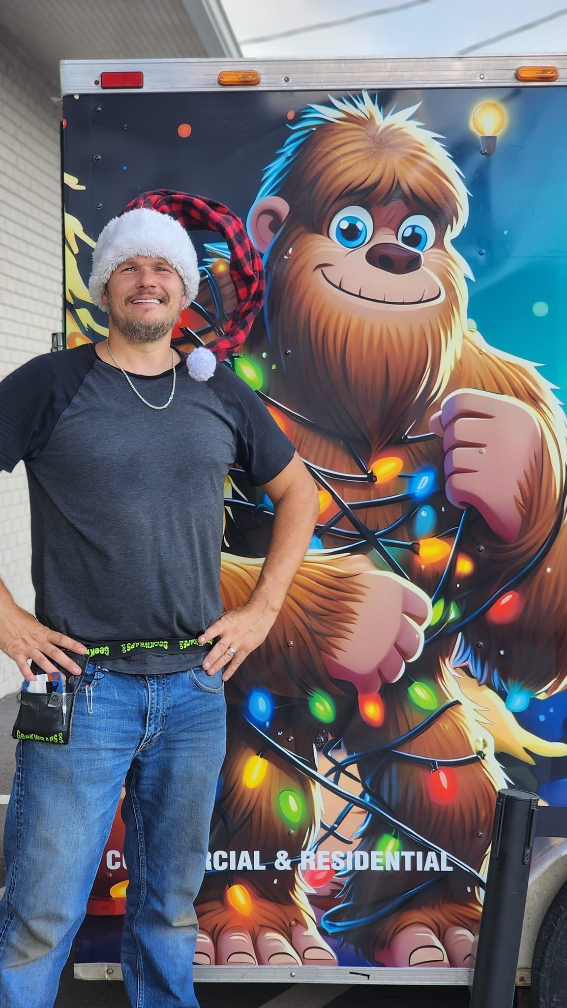 A man wearing a santa hat is standing in front of a christmas truck.
