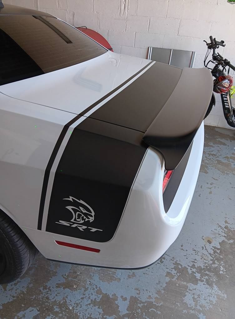 A white dodge challenger with a black and white stripe on the side is parked in a garage.