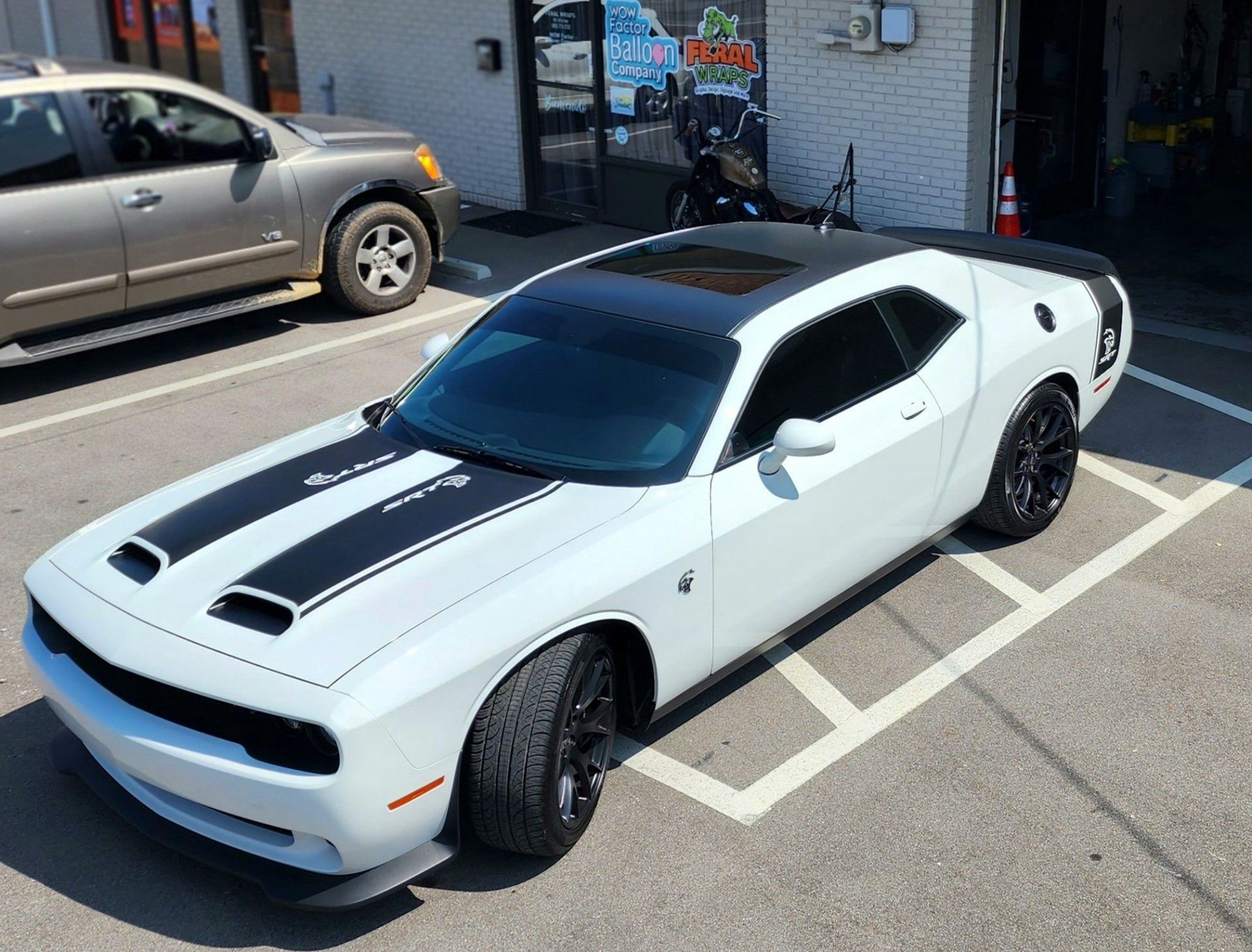 A white dodge challenger with black stripes is parked in a parking lot.