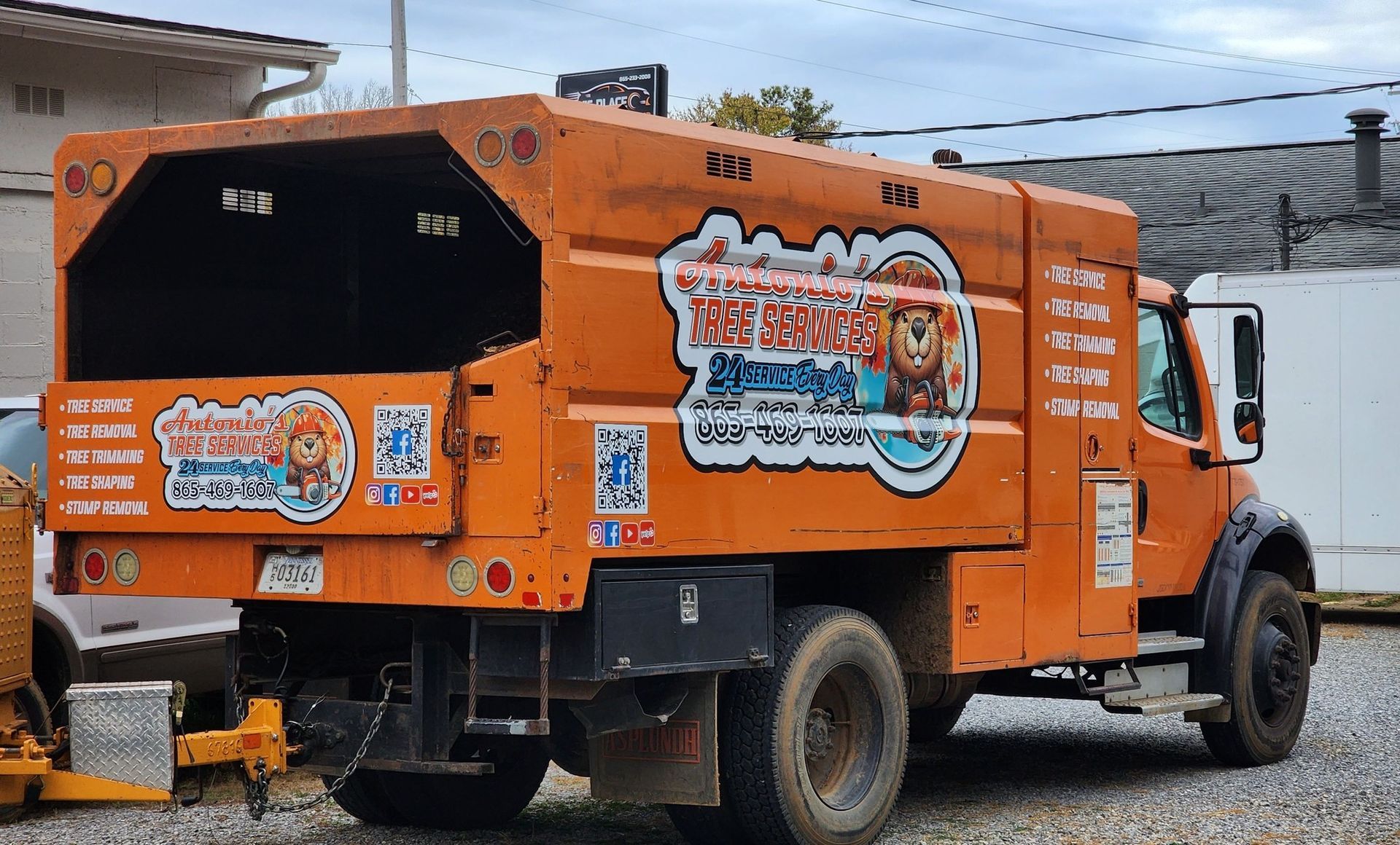 An orange garbage truck is parked in a gravel lot.